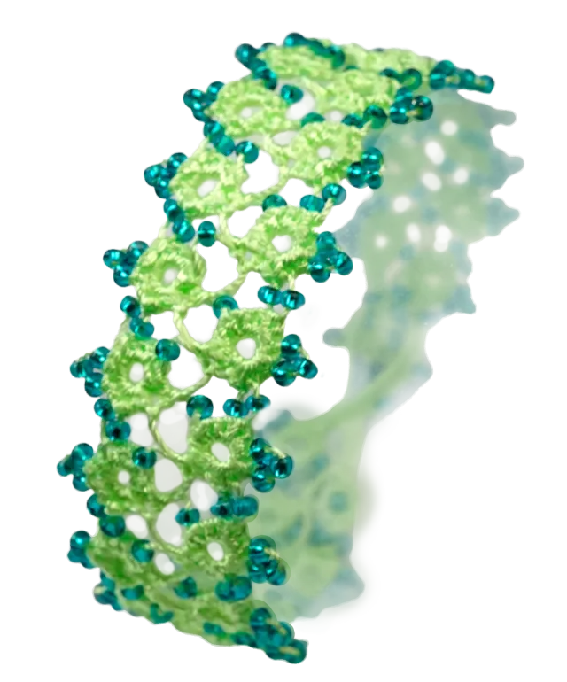 Set of handmade lace textile jewellery placed on pebbles, green and emerald colours