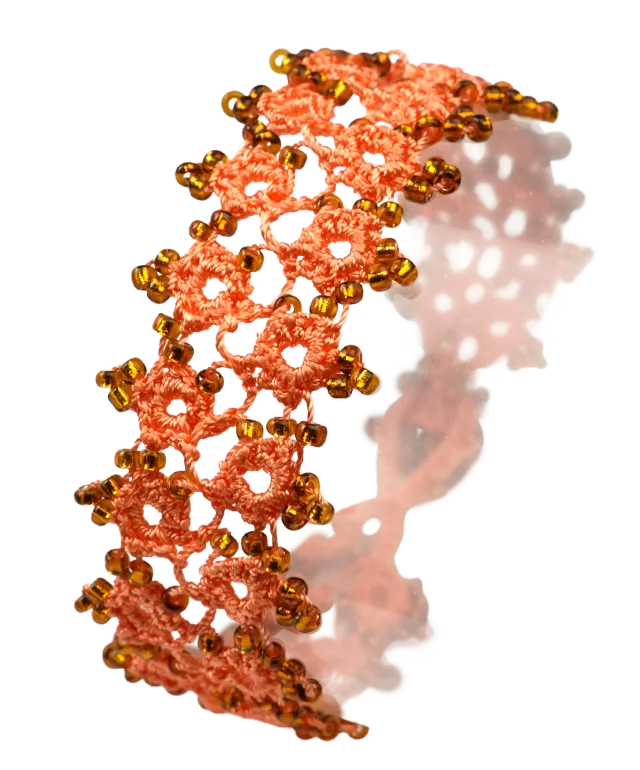 Handmade lace textile bracelet, Husnu, OYA collection, orange and copper colours set on a pebble