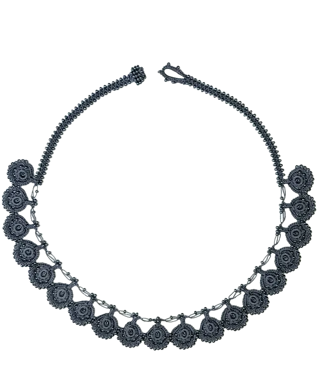 Close-up of Eda necklace in slate blue Oya lace placed on pebbles