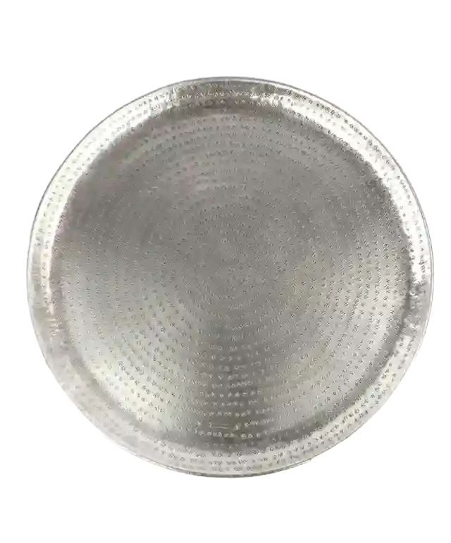 Plateau en laiton argenté martelé et gravé Palmyr posé sur un tabouret en bois, un coussin déco dépassant de la photo