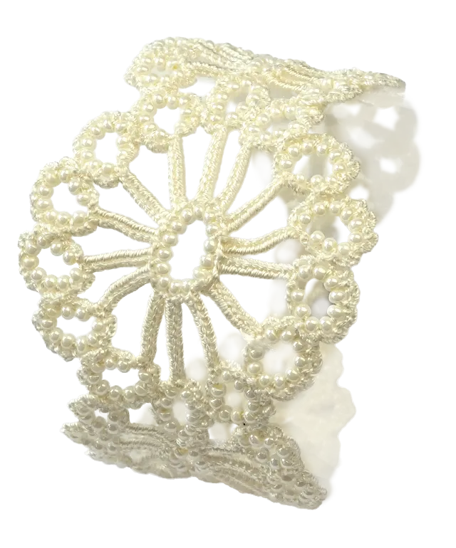 Light ivory Hawa lace bracelet, decorated with pearls, placed on a white pebble