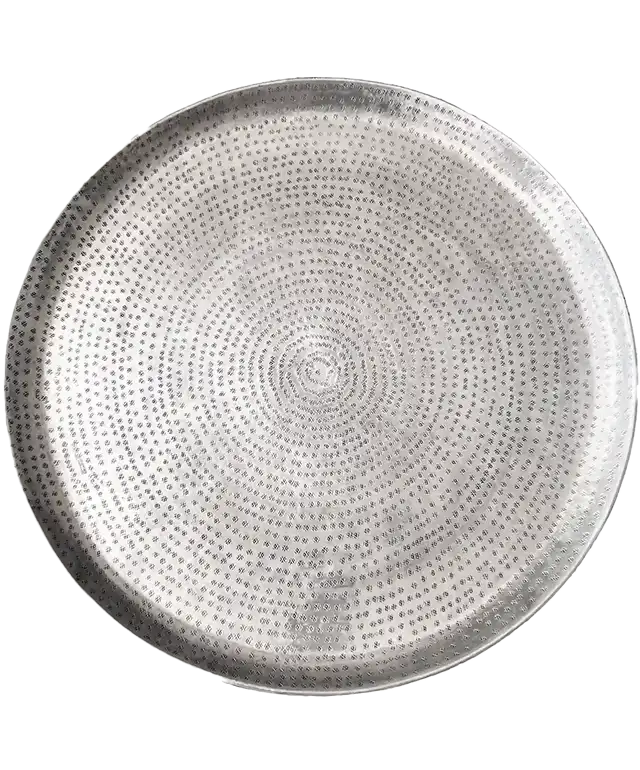 Plateau en laiton argenté martelé et gravé Palmyr posé sur un tabouret en bois, un coussin déco dépassant de la photo