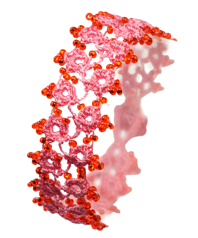 Handmade lace textile bracelet, Husnu, OYA collection, pink and red colours placed on a pebble