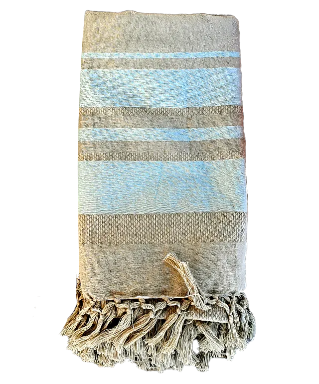 Earth beige organic cotton fouta suspended and floating lightly in the wind with a sandy beach and the sea in the background