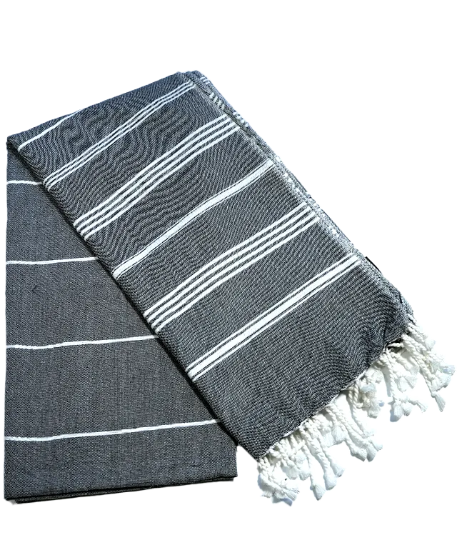 Femme portant une fouta anthracite en coton bio de la collection Hammam, devant une plage