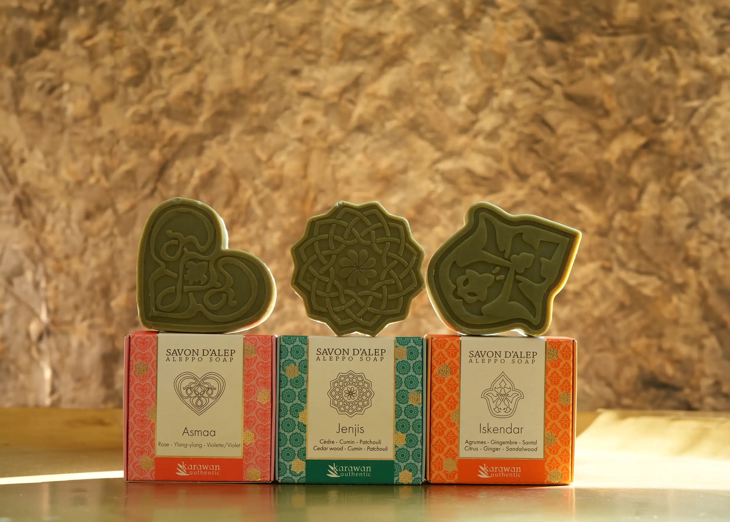 Trois savons d'Alep parfumés aux fragrances naturelles, exposés sur leurs coffrets respectifs