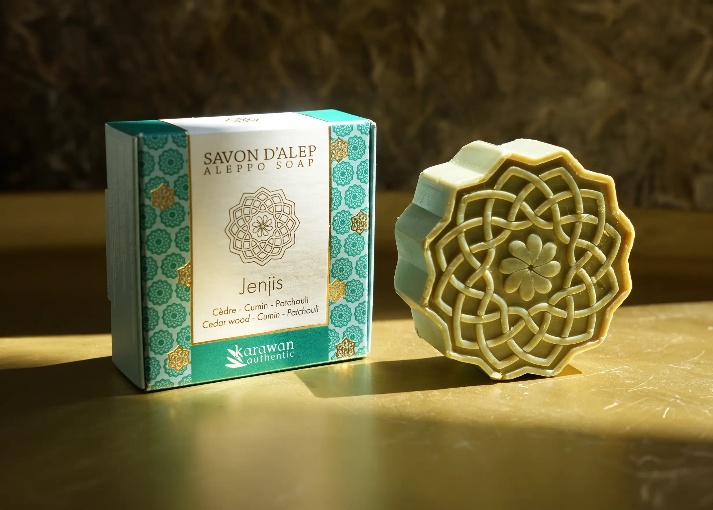 Savon d'Alep parfumé Jenjis, en forme de fleurs et à la senteur boisée, à côté de son écrin doré