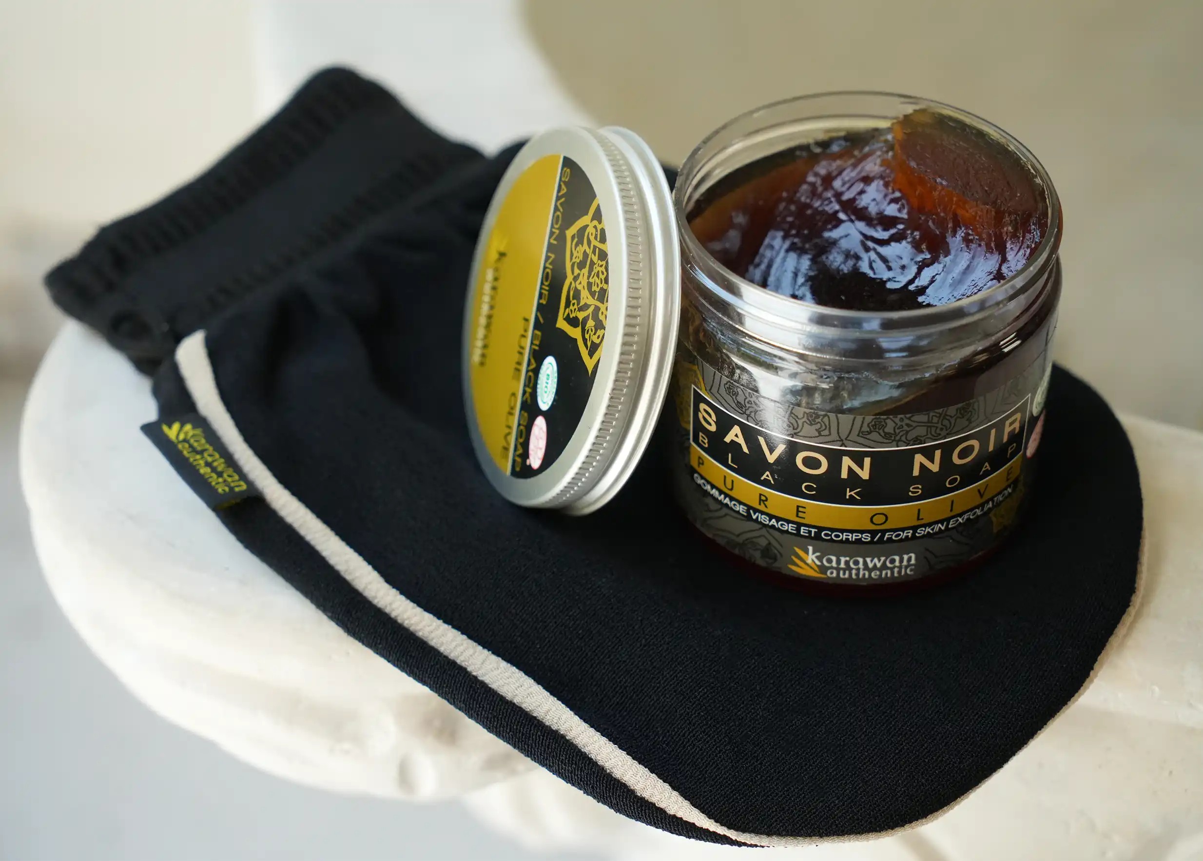 Pot of black soap opened on a kessa glove, showing the texture of the soap