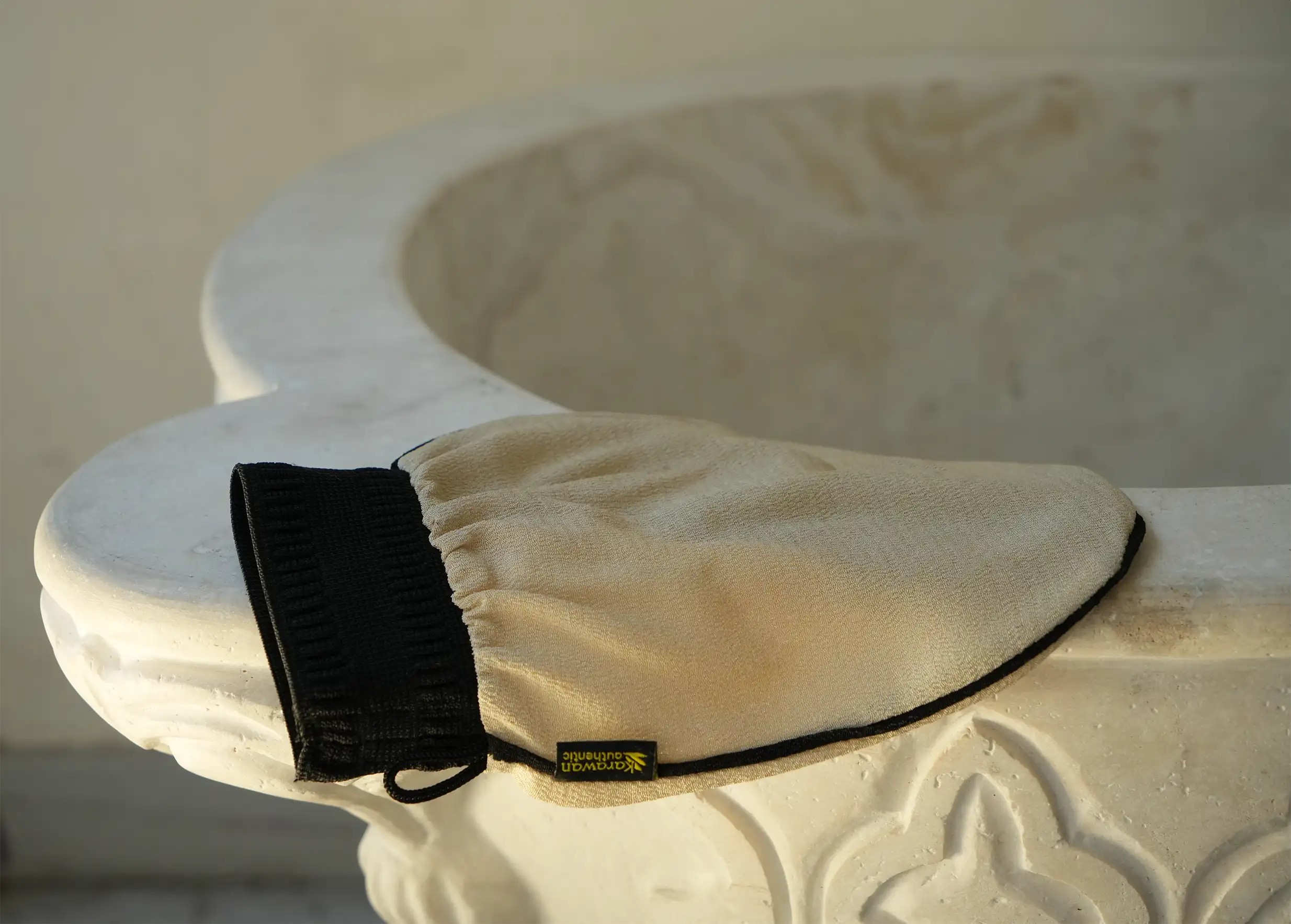 Kessa scrubbing glove, beige and black, resting on a rim