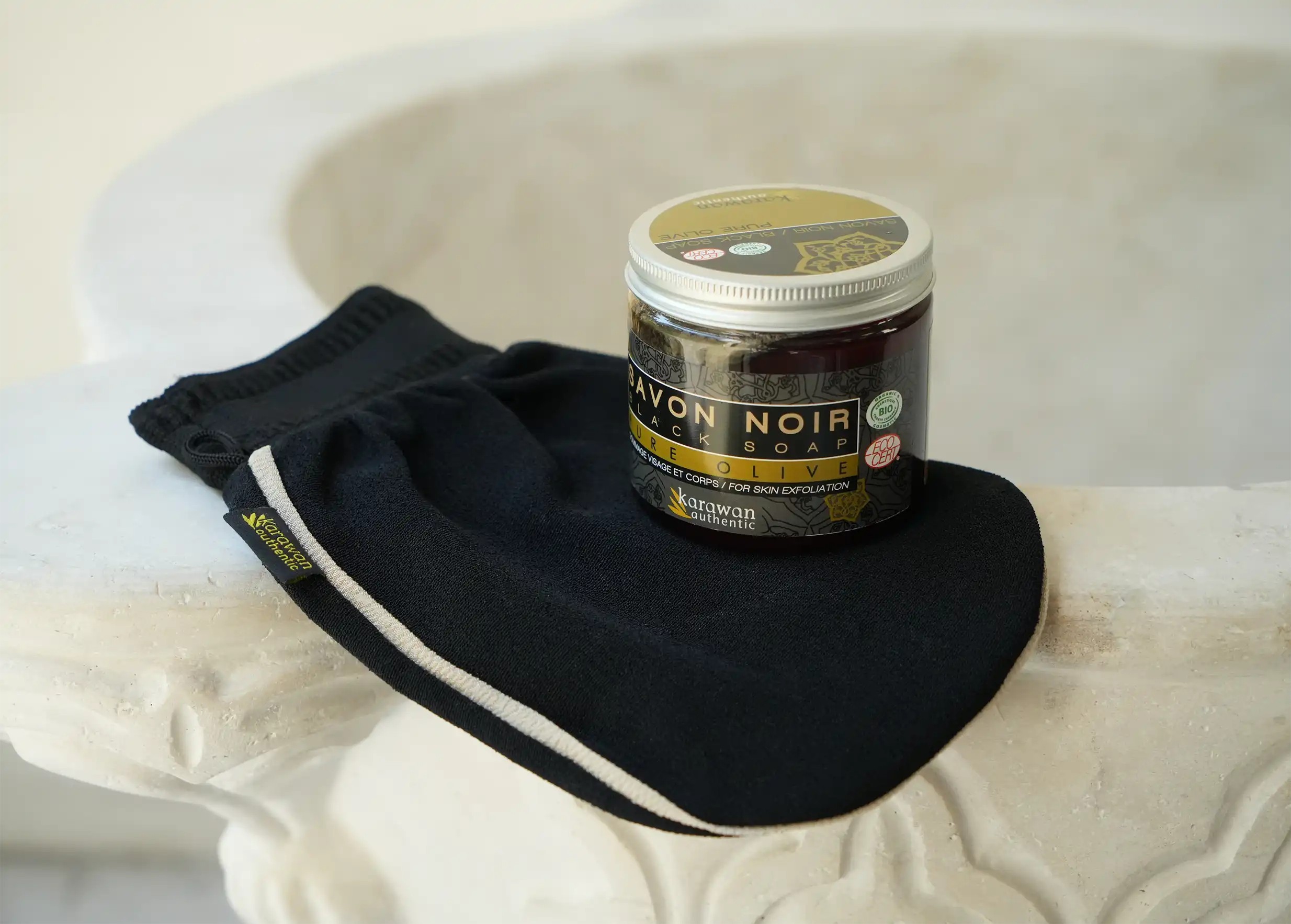 Handmade pot of pure olive authentic black soap on a black kessa scrubbing glove