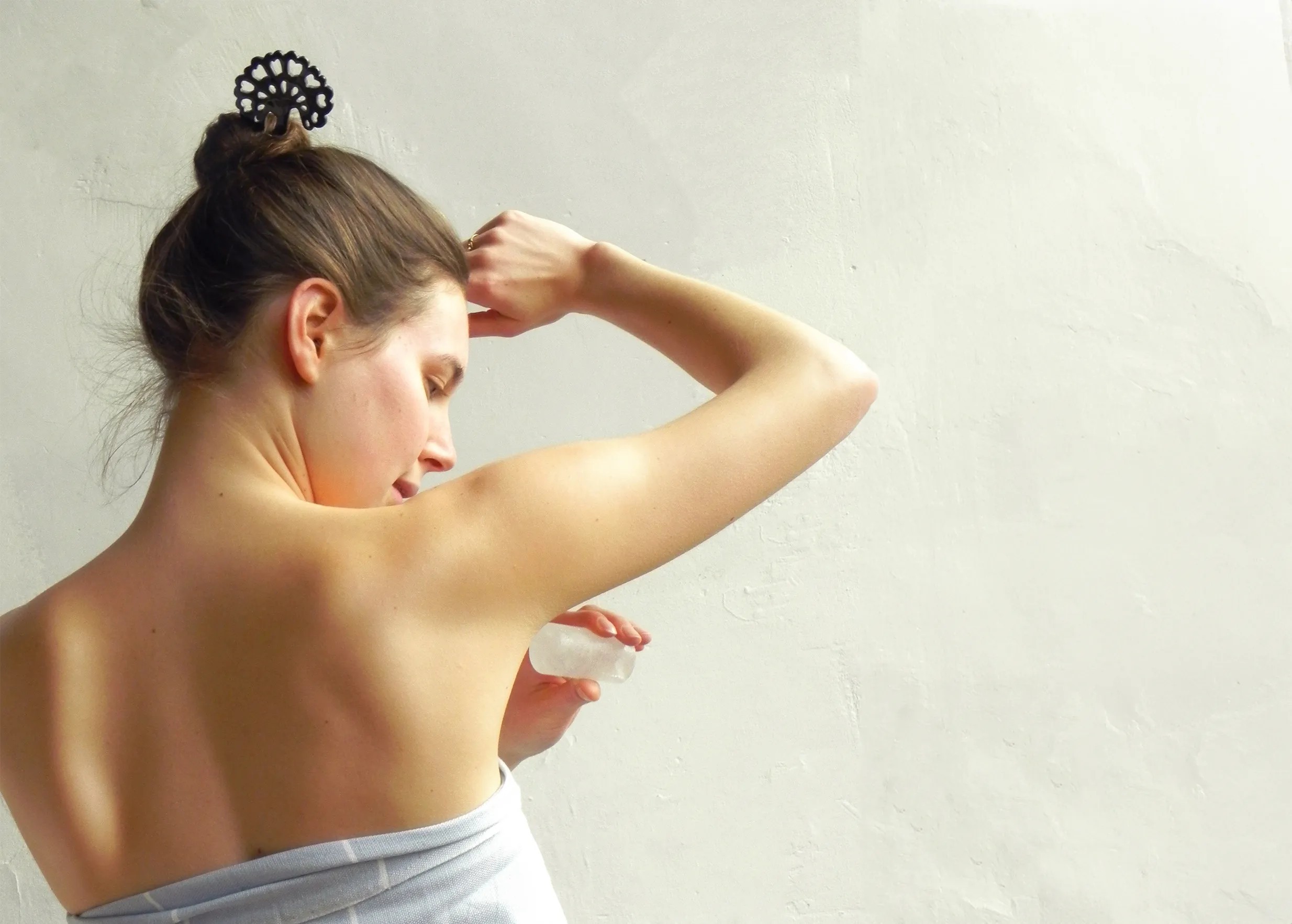 Woman seen from behind applying an alum stone stick under her arm