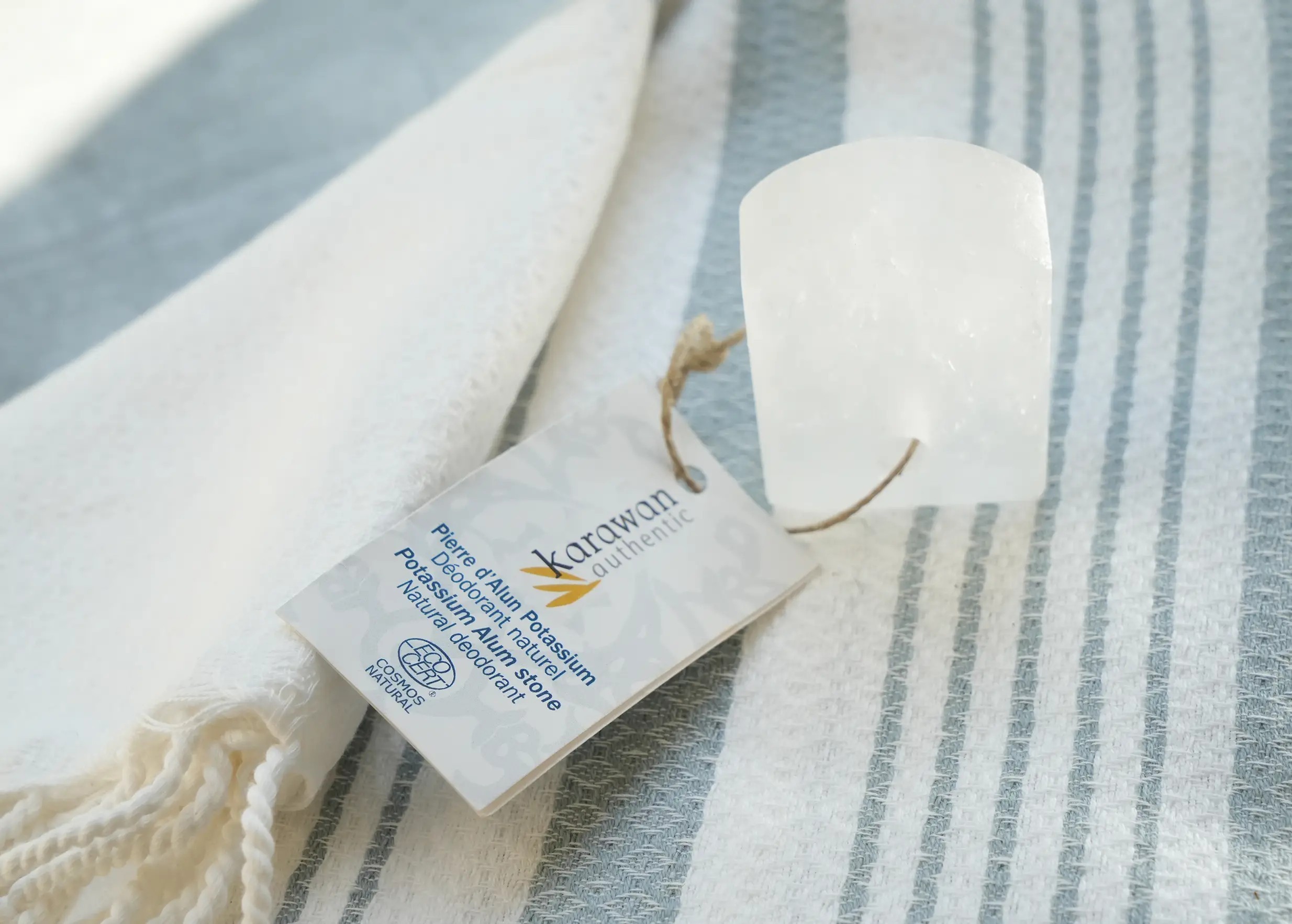 Certified raw polished alum stone with label, on a striped fouta
