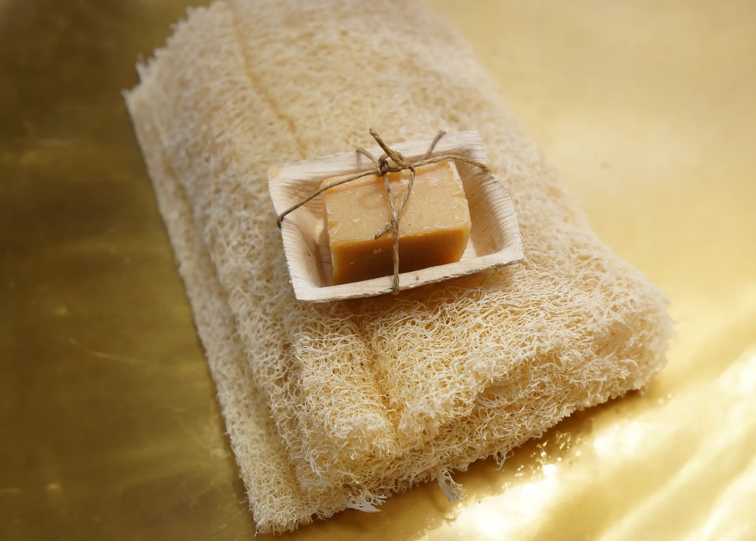 Natural handmade soap wrapped with string, placed on a loofah sponge, all presented on a golden background