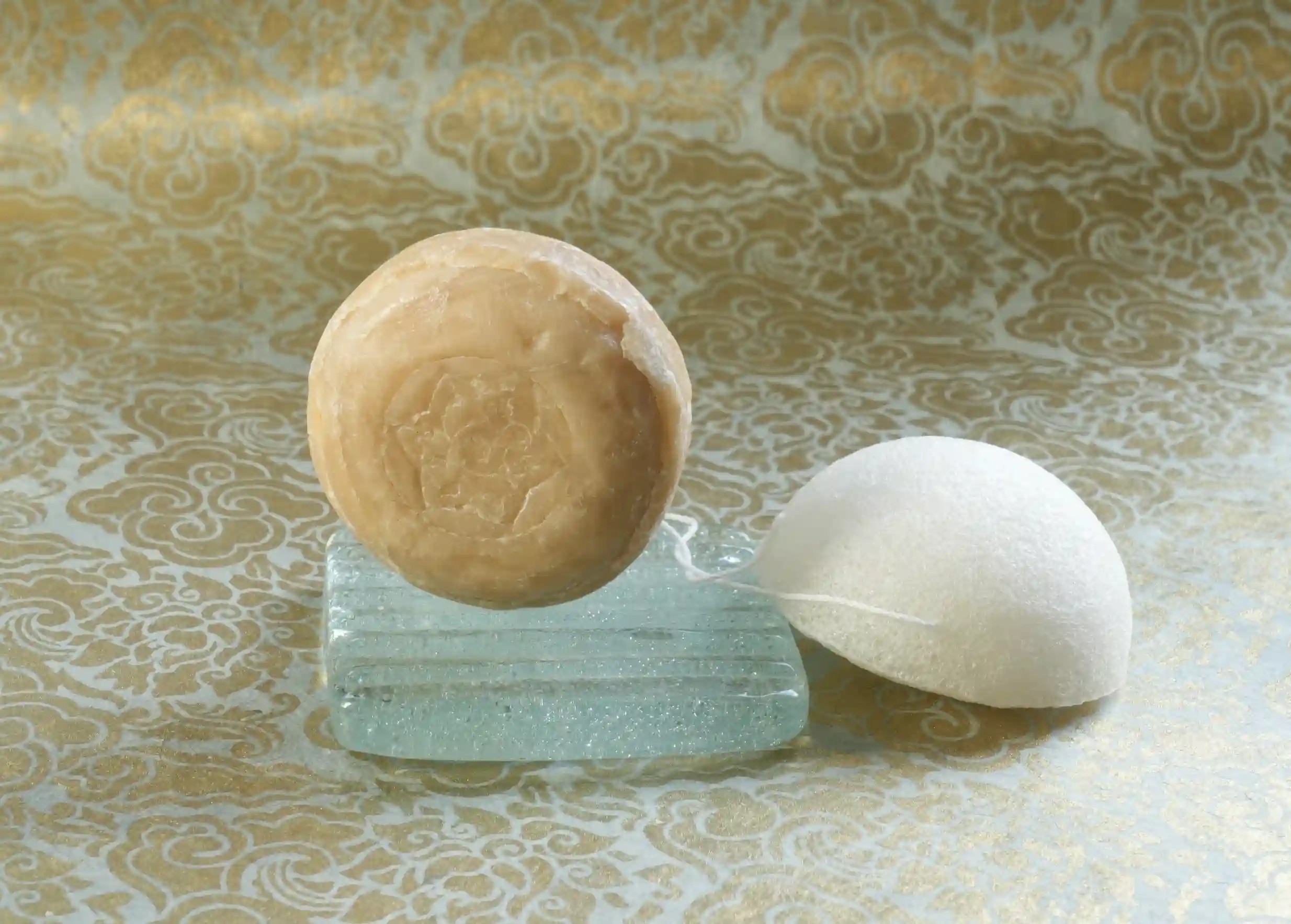 Softening care set with ayurvedic holy basil soap on a glass soap dish, and plant-based konjac sponge