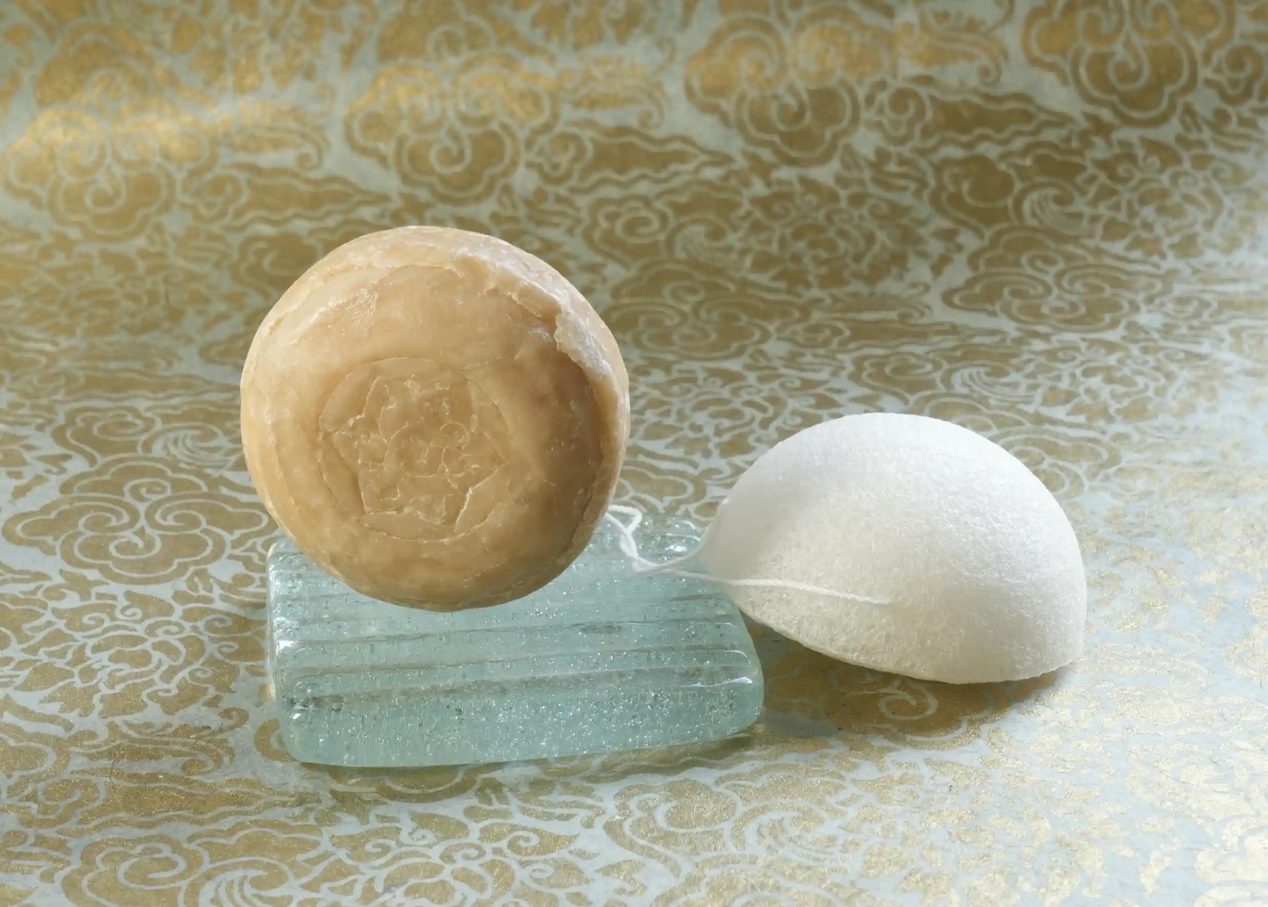 Regenerating care set with ayurvedic bergamot soap on a glass soap dish, and vegetable konjac sponge
