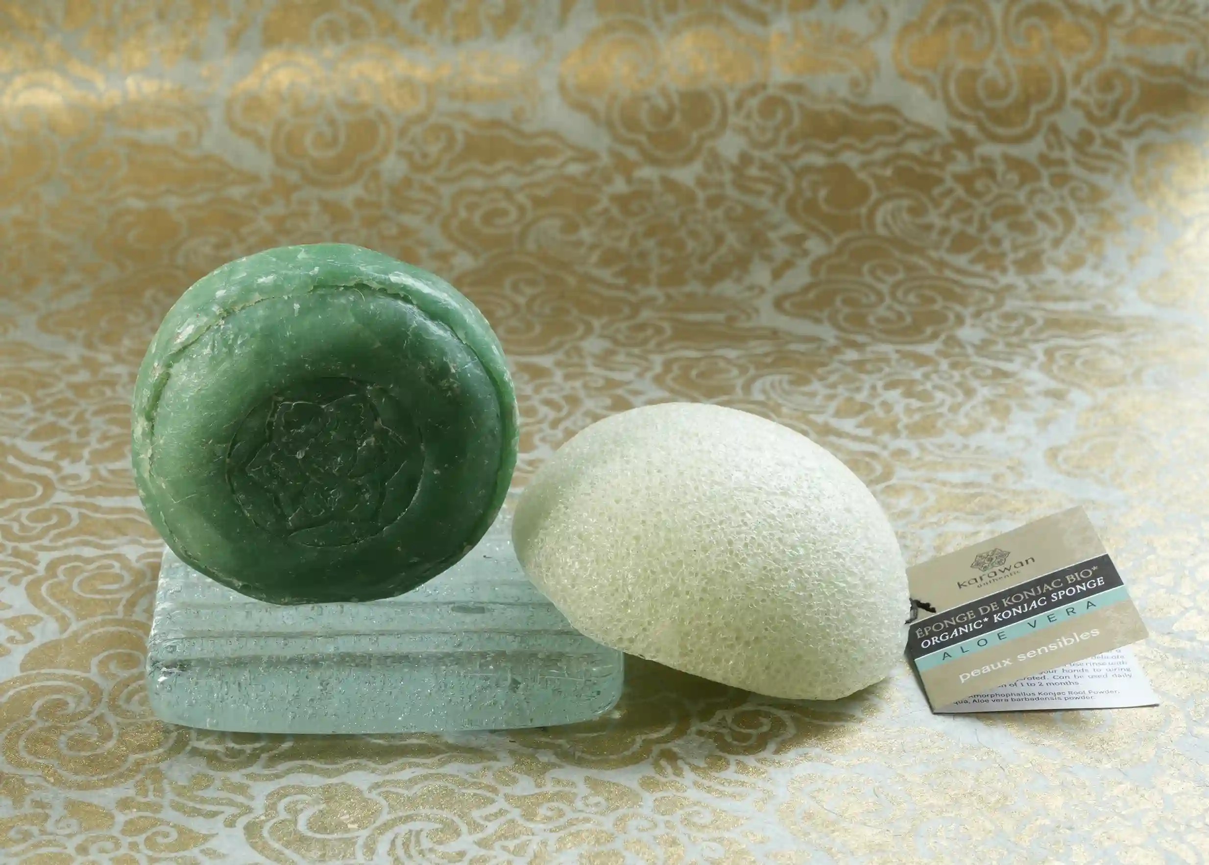 Savon ayurvédique rond au vétiver sur un porte savon en verre, et éponge konjac enrichie à l'aloe vera