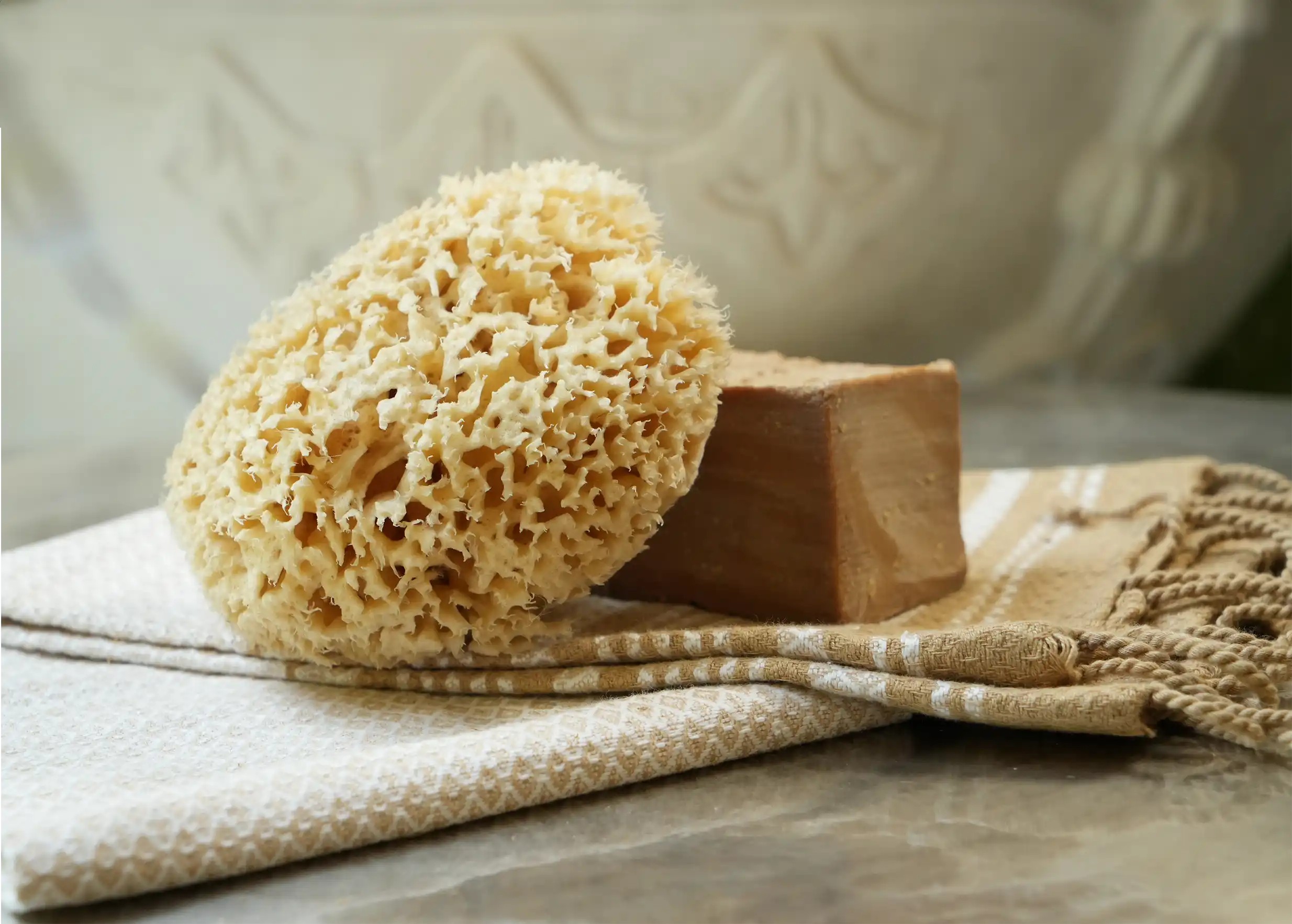 Éponge de mer naturelle contre un savon d'Alep authentique, sur une fouta en coton bio dotée de franges