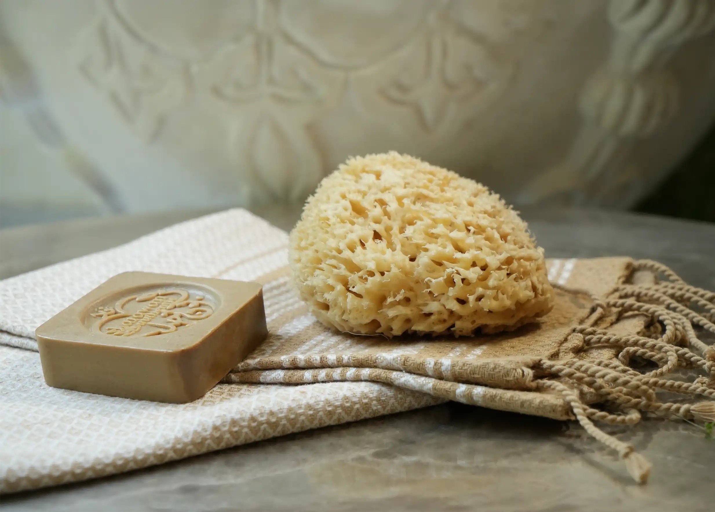 Éponge de mer naturelle et savon d'Alep tamponné Karawan authentic sur une fouta en coton bio