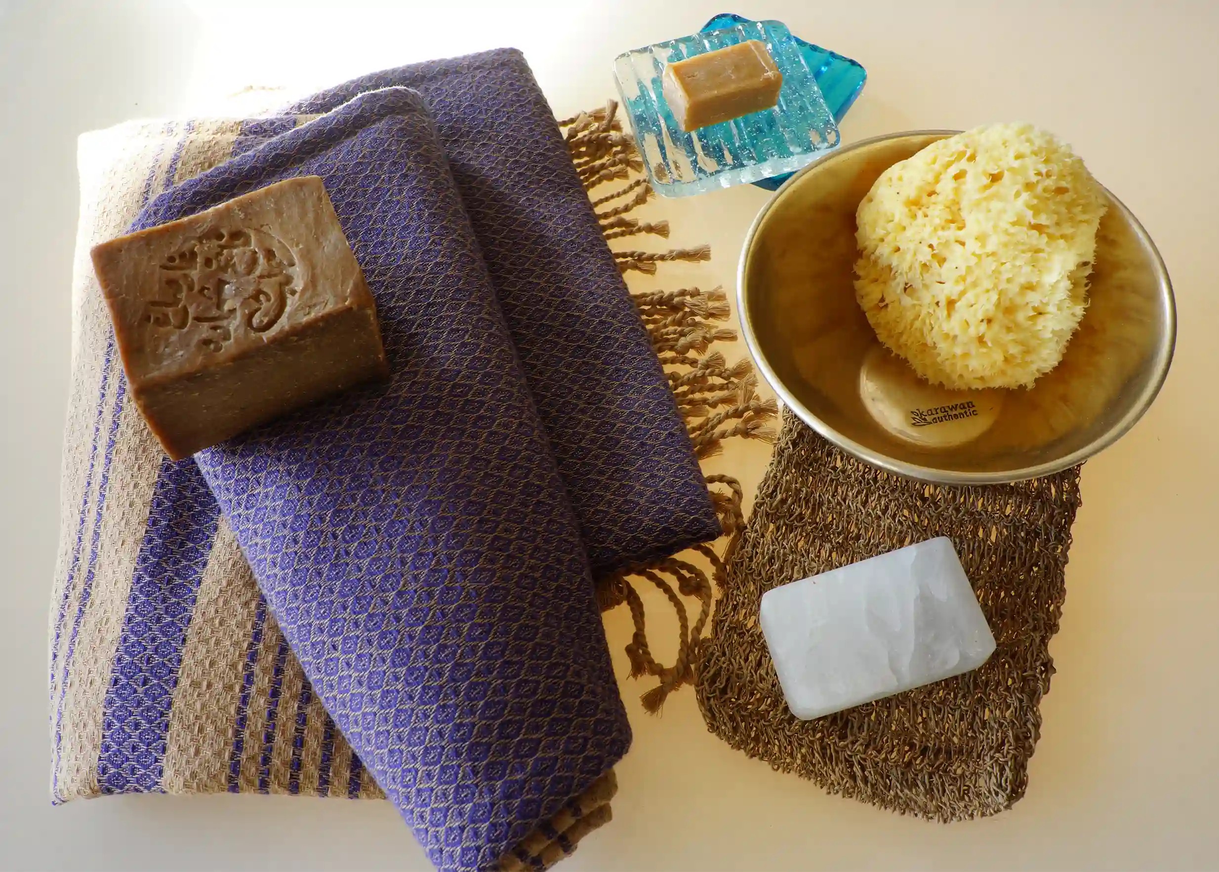 Pierre d'alun rectangulaire, éponge de mer naturelle, mini-savon sur porte savon en verre, et savon d'Alep sur fouta bleue