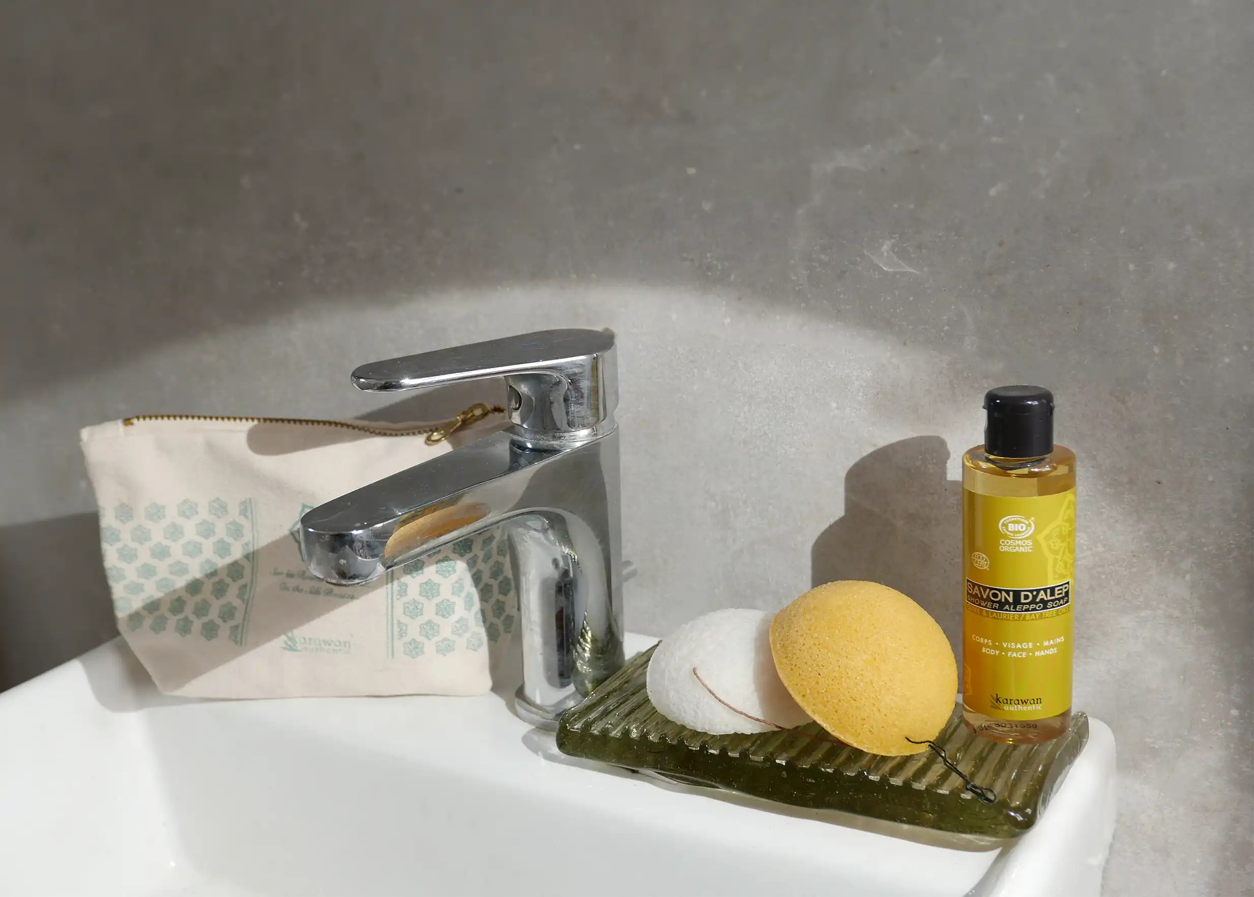Éponge de konjac bio au curcuma et éponge naturelle près d'une trousse de toilette et d'un savon d'Alep liquide Karawan