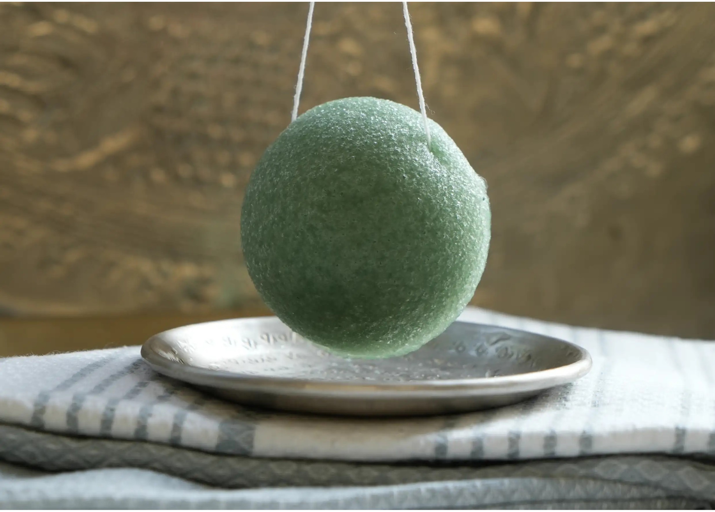 Éponge de konjac enrichie à l'aloe vera suspendue au dessus d'une coupelle en laiton argenté