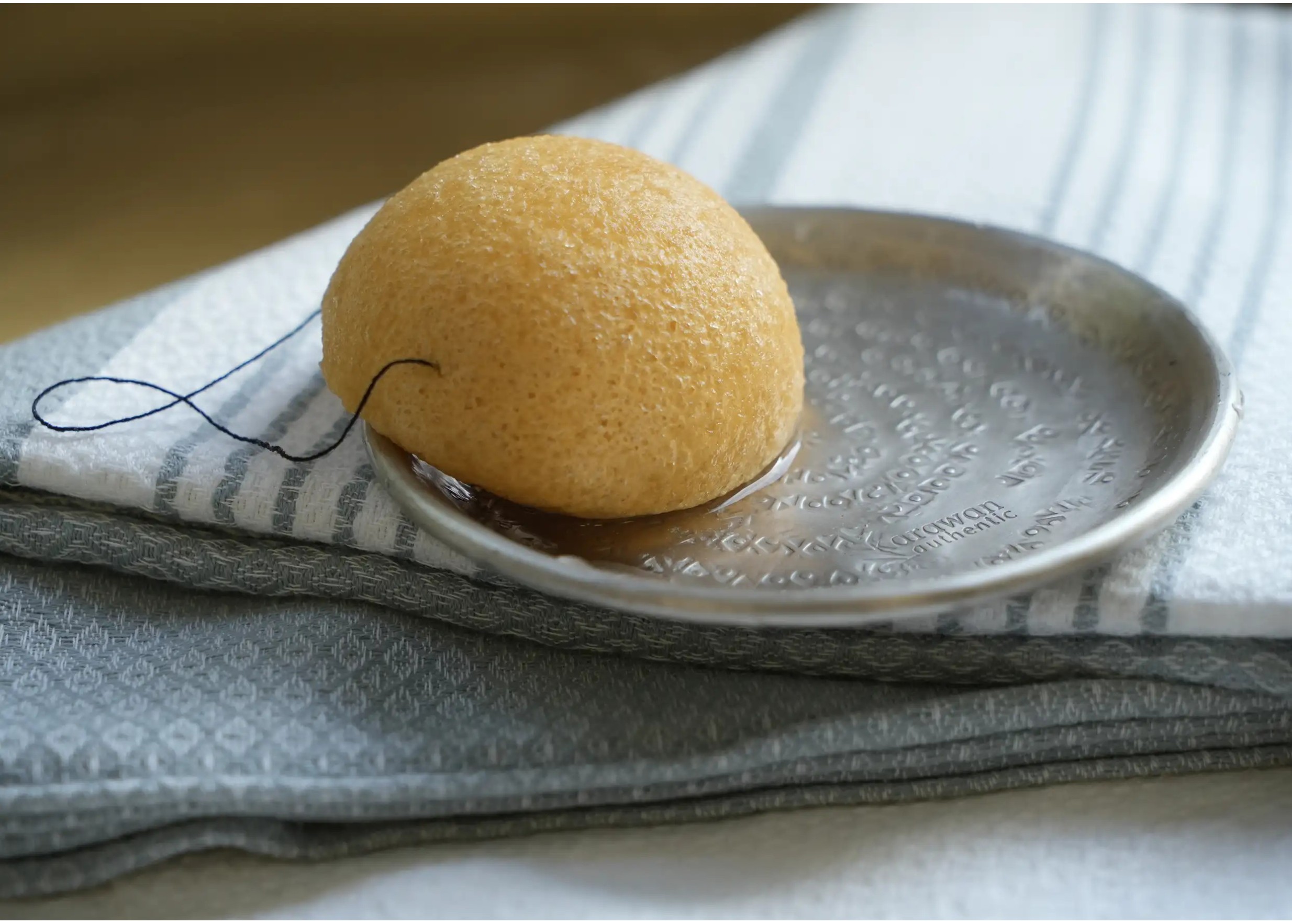 Éponge konjac au curcuma légèrement humidifée, sur une coupelle en laiton disposée sur une fouta