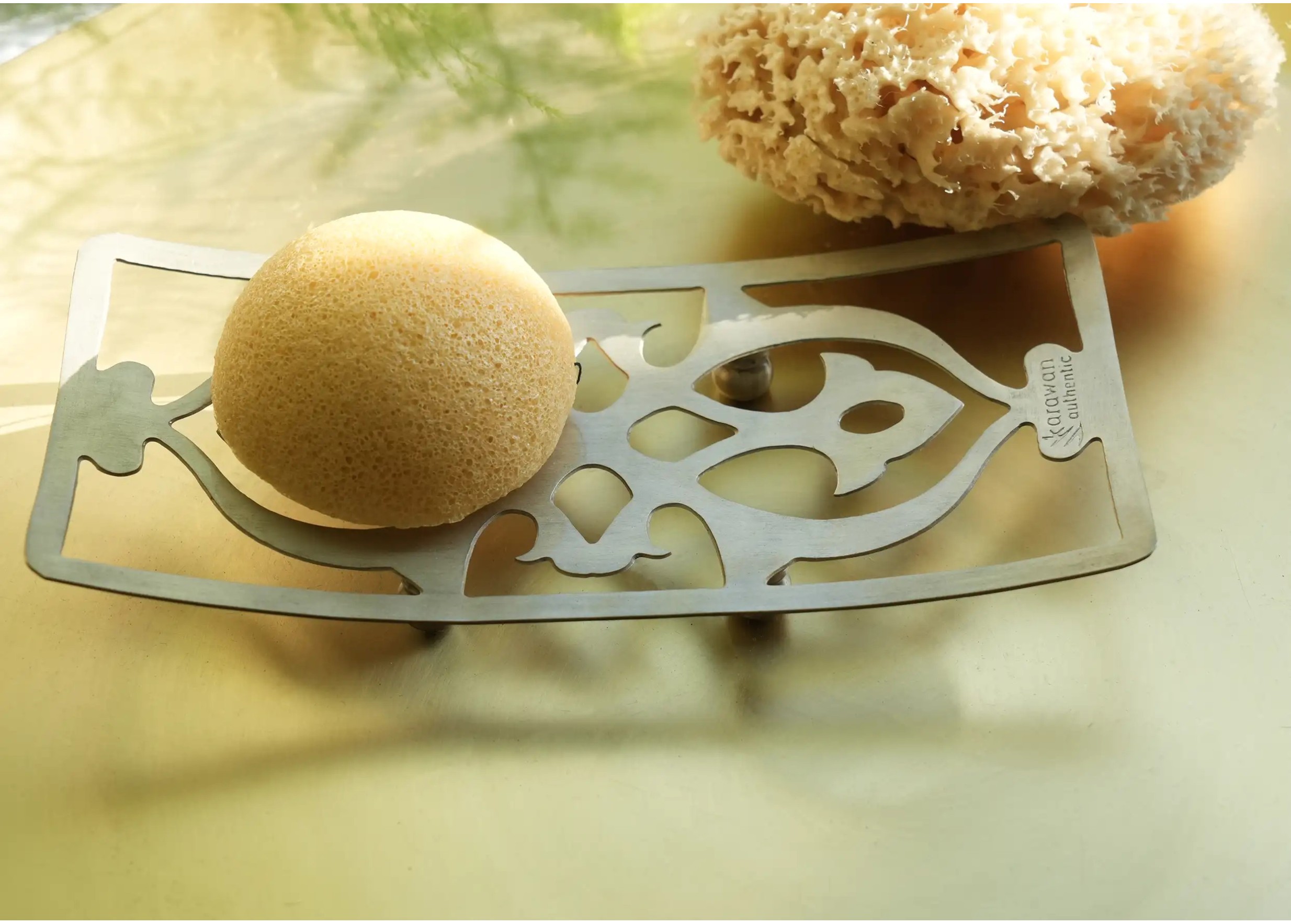 Éponge de mer naturelle et éponge konjac à proximité d'un support d'accessoires de bain en laiton Nairi
