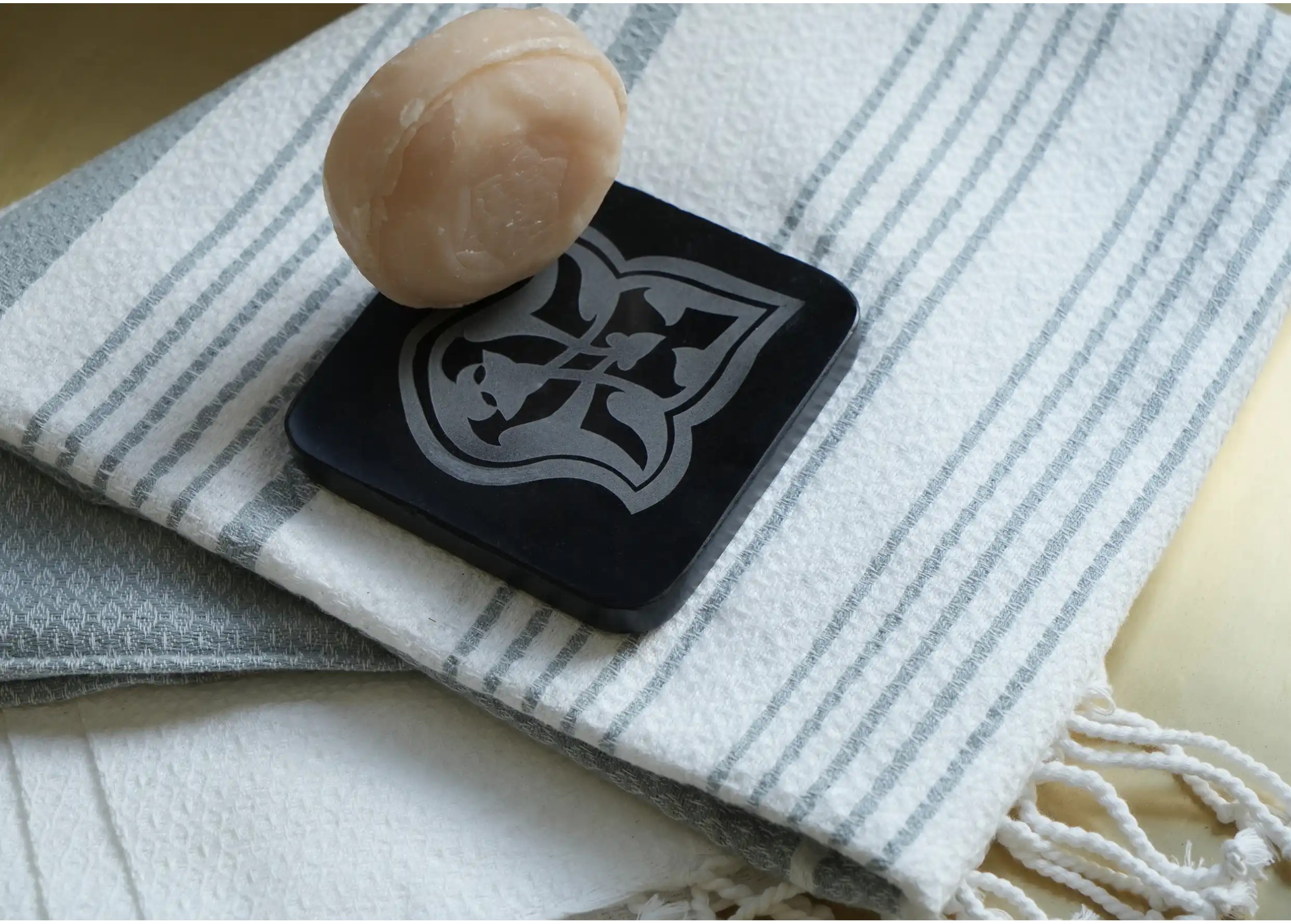 Porte savon en marbre noir posé sur une fouta rayée en coton bio, sur ce porte-savon un savon rond ayurvédique