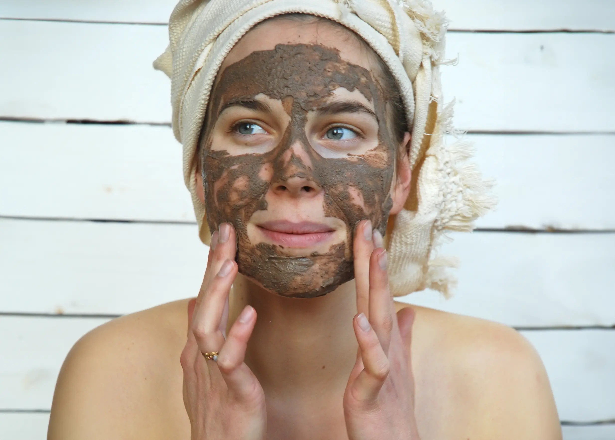 Woman applying a clay mask to her face, rhassoul powder