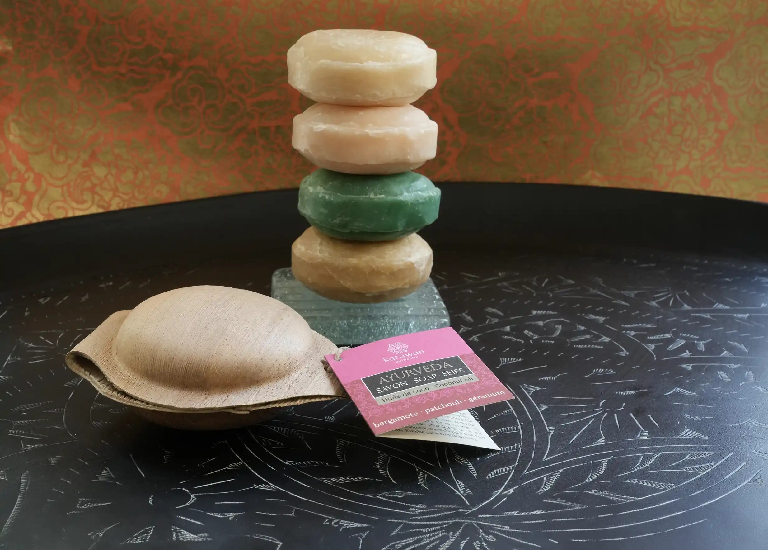 Ayurvedic soap with its eopackaging, stack of circular soaps in the background, all on a brass tray