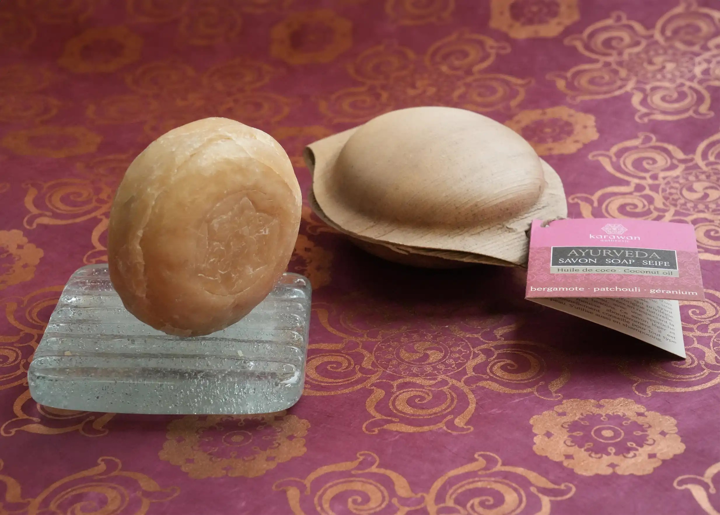 Round solid soap with bergamot fragrance and Karawan design, on a soap dish, and soap in its palm leaf shell
