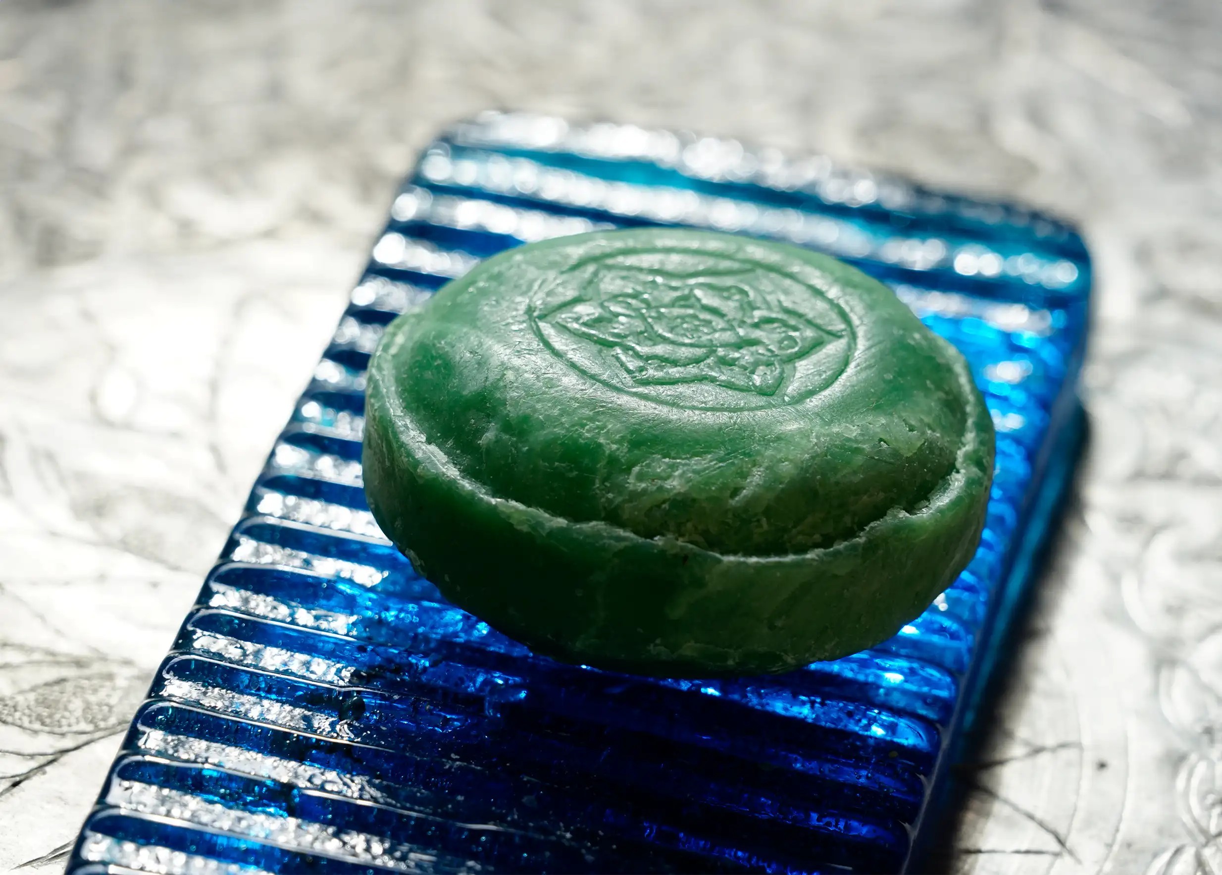 Savon ayurvédique au vétiver de forme ronde, avec un motif de rosace tamponné, sur un porte savon en verre bleu