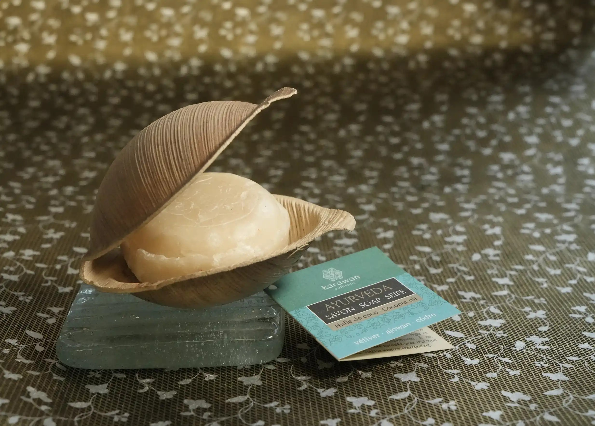 Savon ayurvédique vétiver 100g dans sa coque végétale, sur un porte savon en verre, et étiquette carton