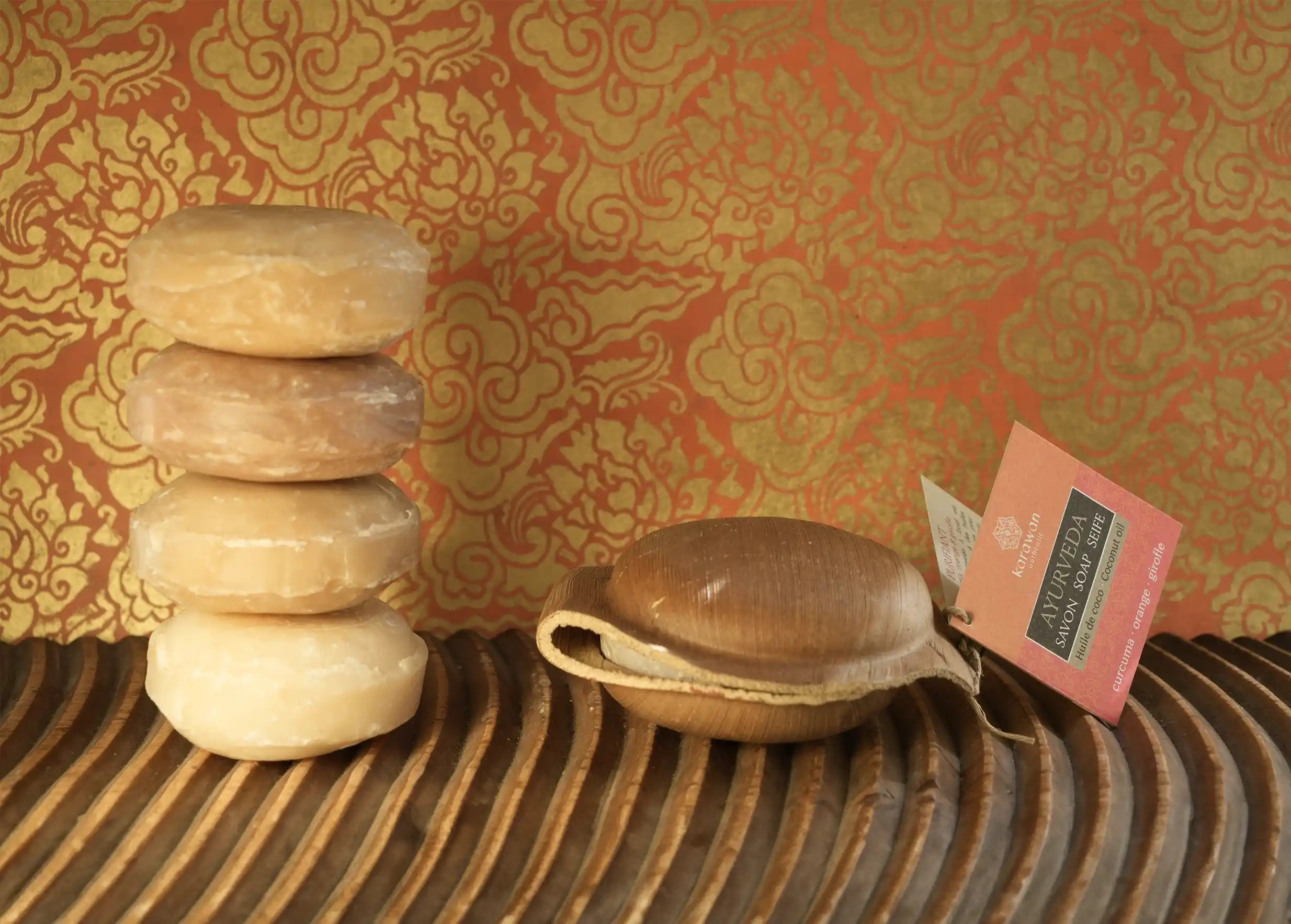 Stack of four round Ayurvedic soaps and one soap packaged in a natural container with Karawan label