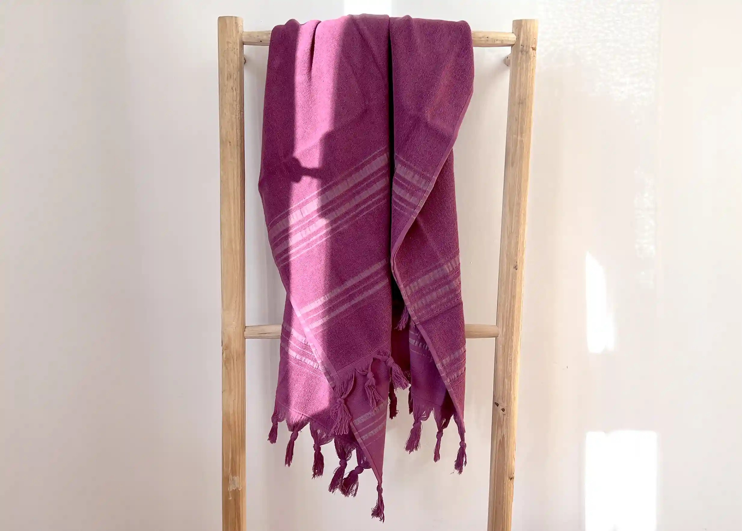 Fouta en coton bio violette avec face éponge, accrochée à un support en bois