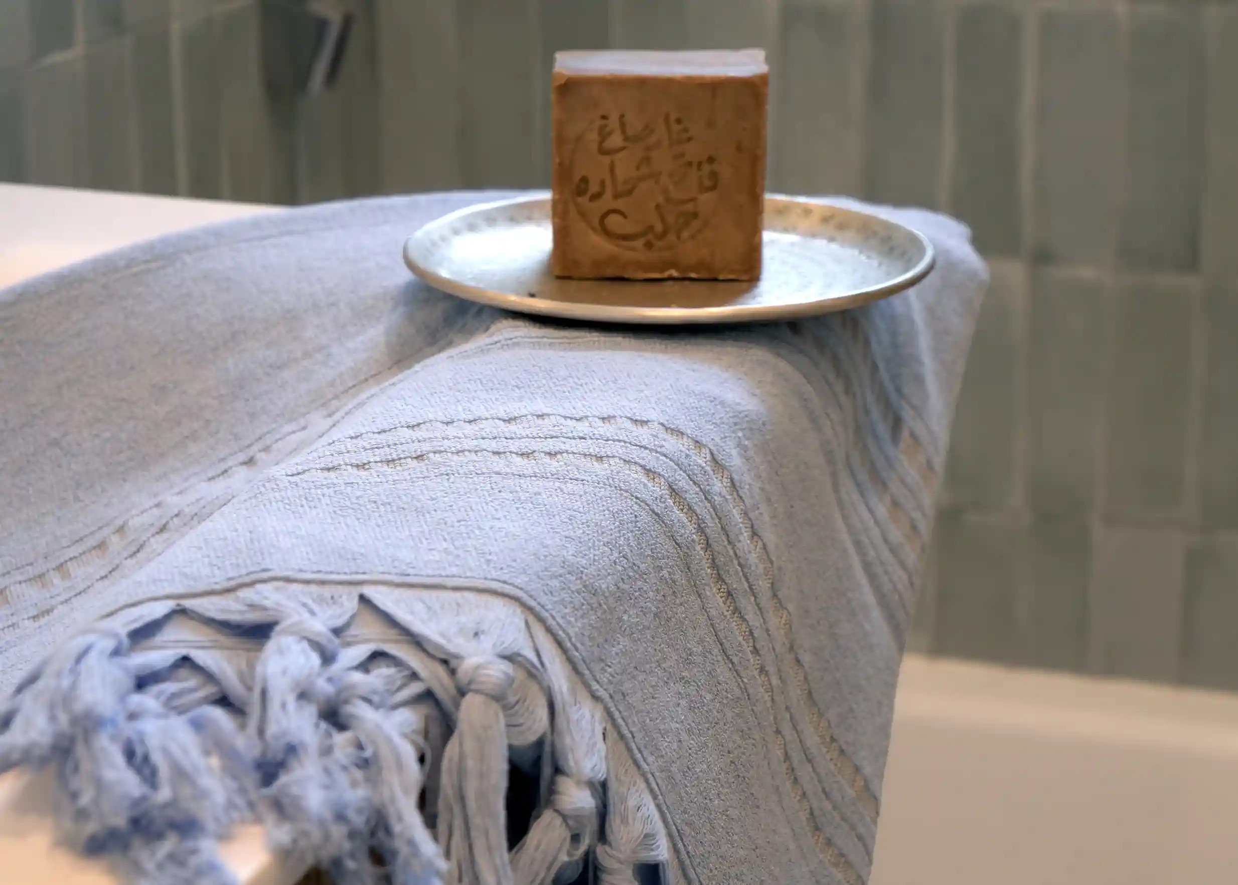 Dolce fouta azurine pliée, avec des franges, savon d'Alep et autres accessoires dans une salle de bain