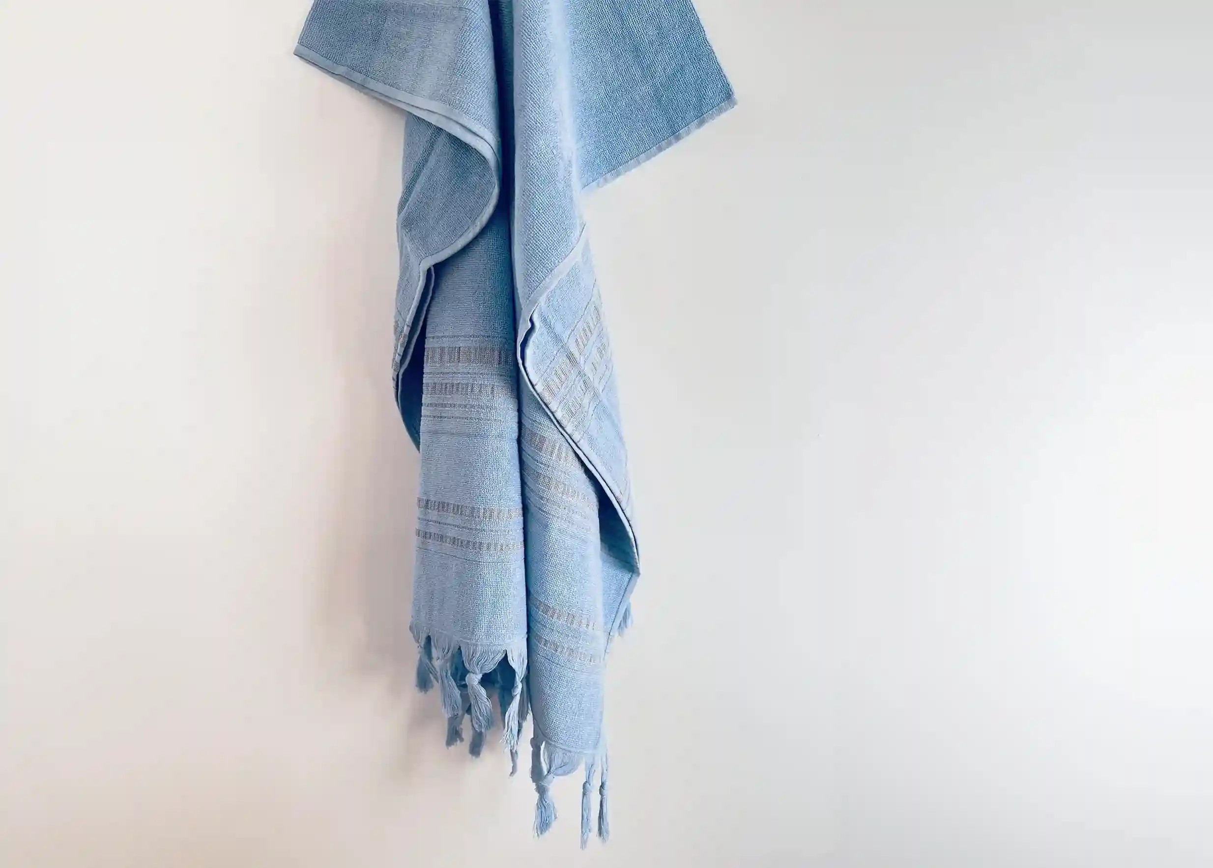 Dolce fouta azurine, aux franges nouées à la main, accrochée à un mur blanc