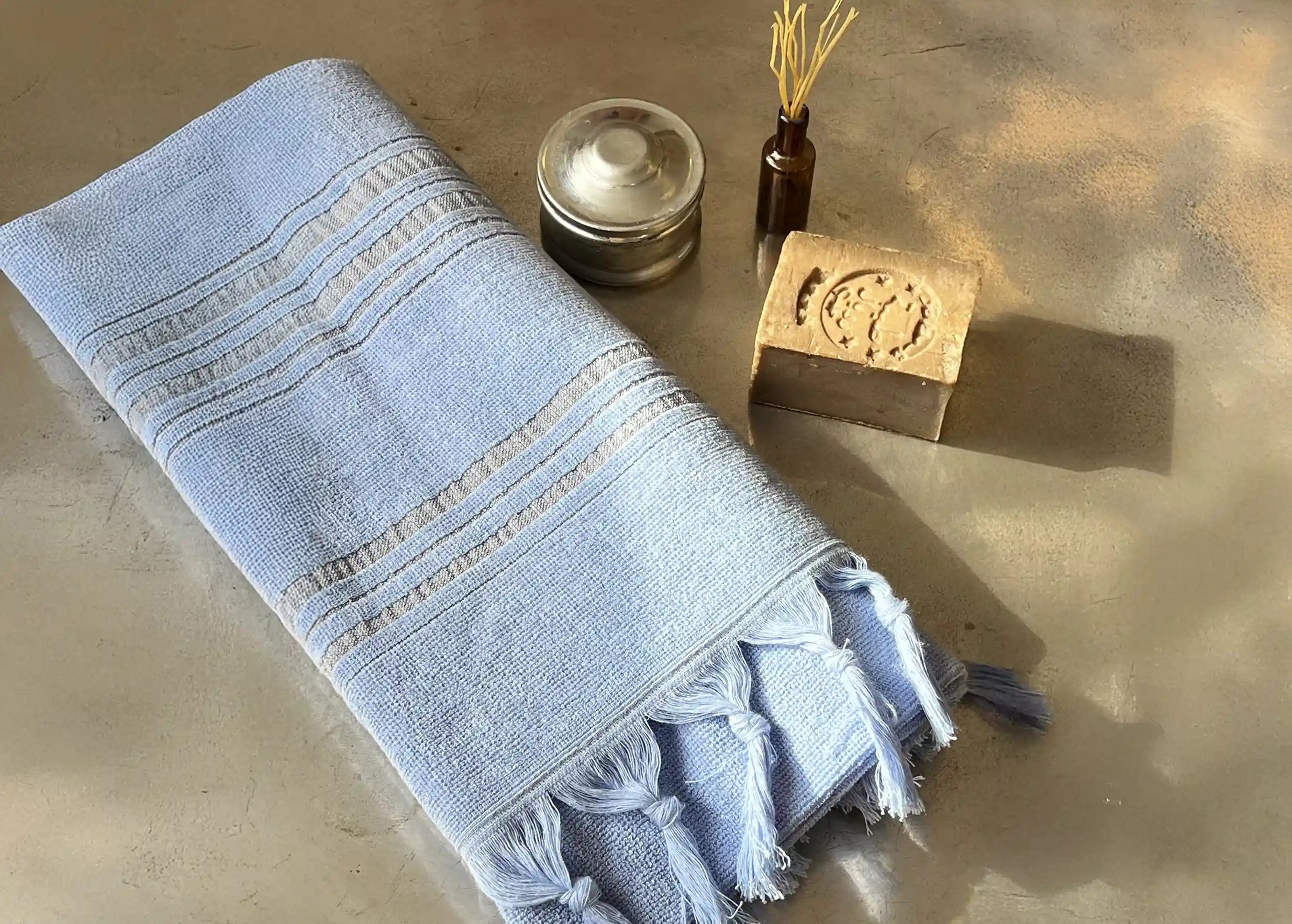 Dolce fouta en coton bio Azurine, accompagnée d'un savon d'Alep dans un bol, tous deux posés sur un plateau en laiton