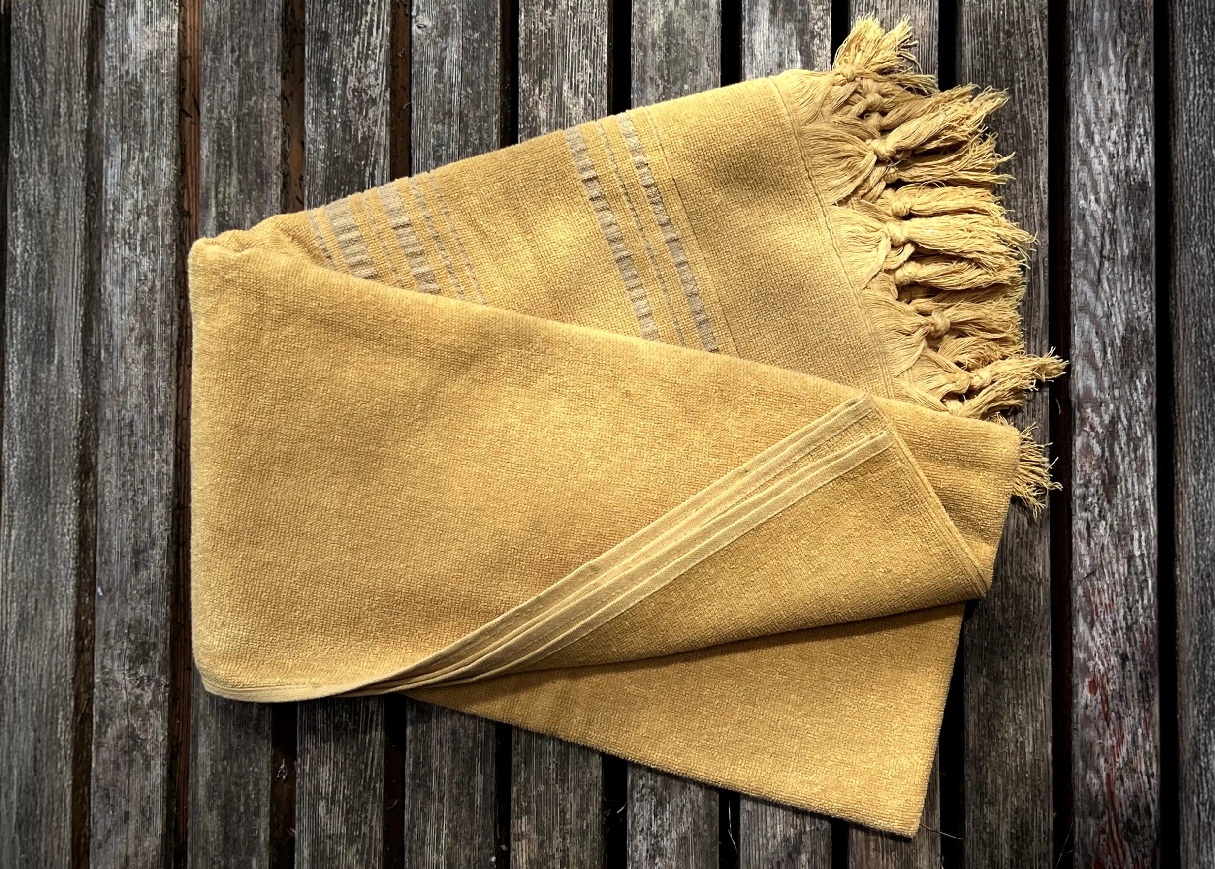 Dolce Fouta en coton bio coloris citrine pliée sur une surface en bois