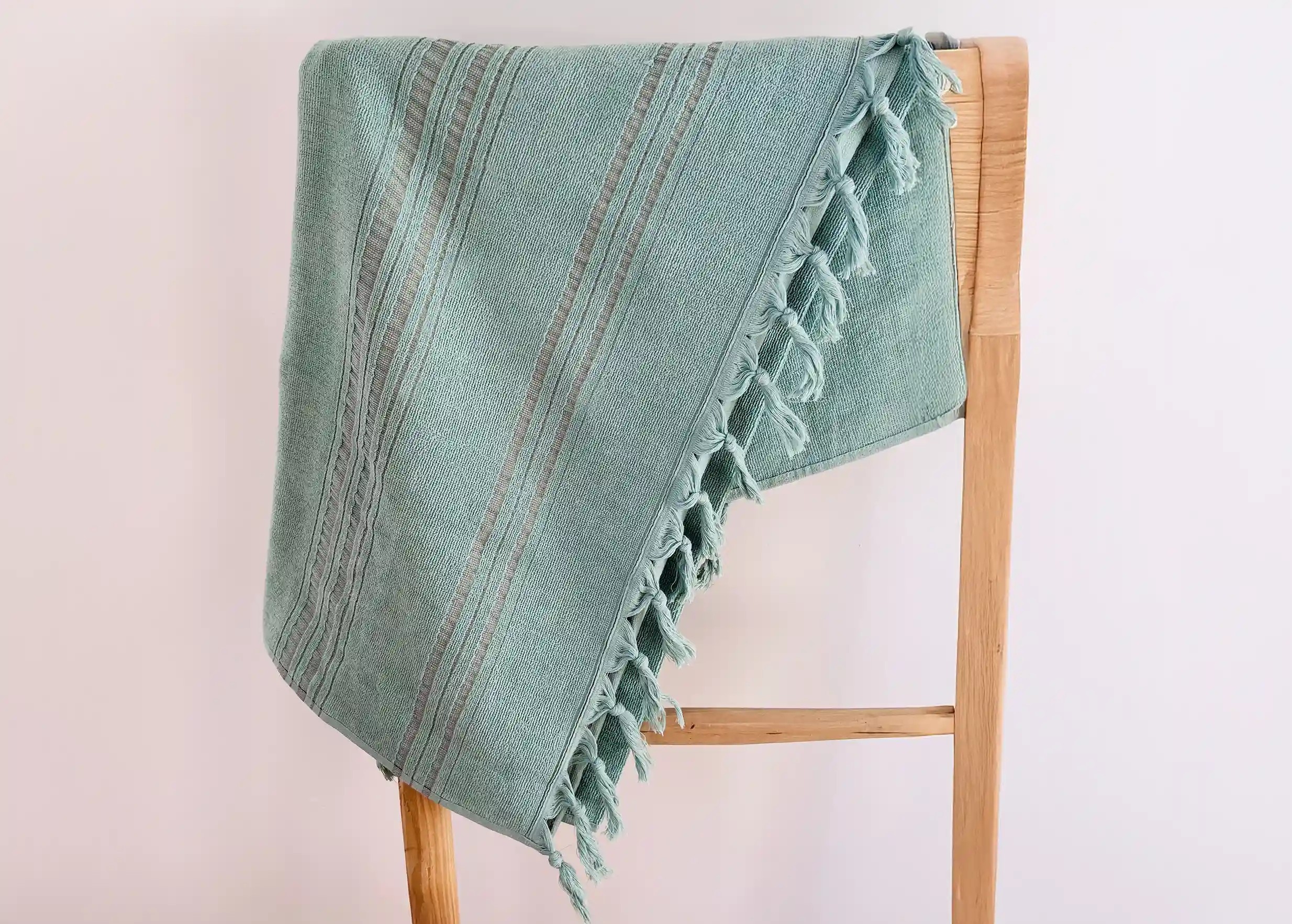 Fouta rayée, coloris jade, posée sur un support en bois, une ombre qui se reflète sur le mur