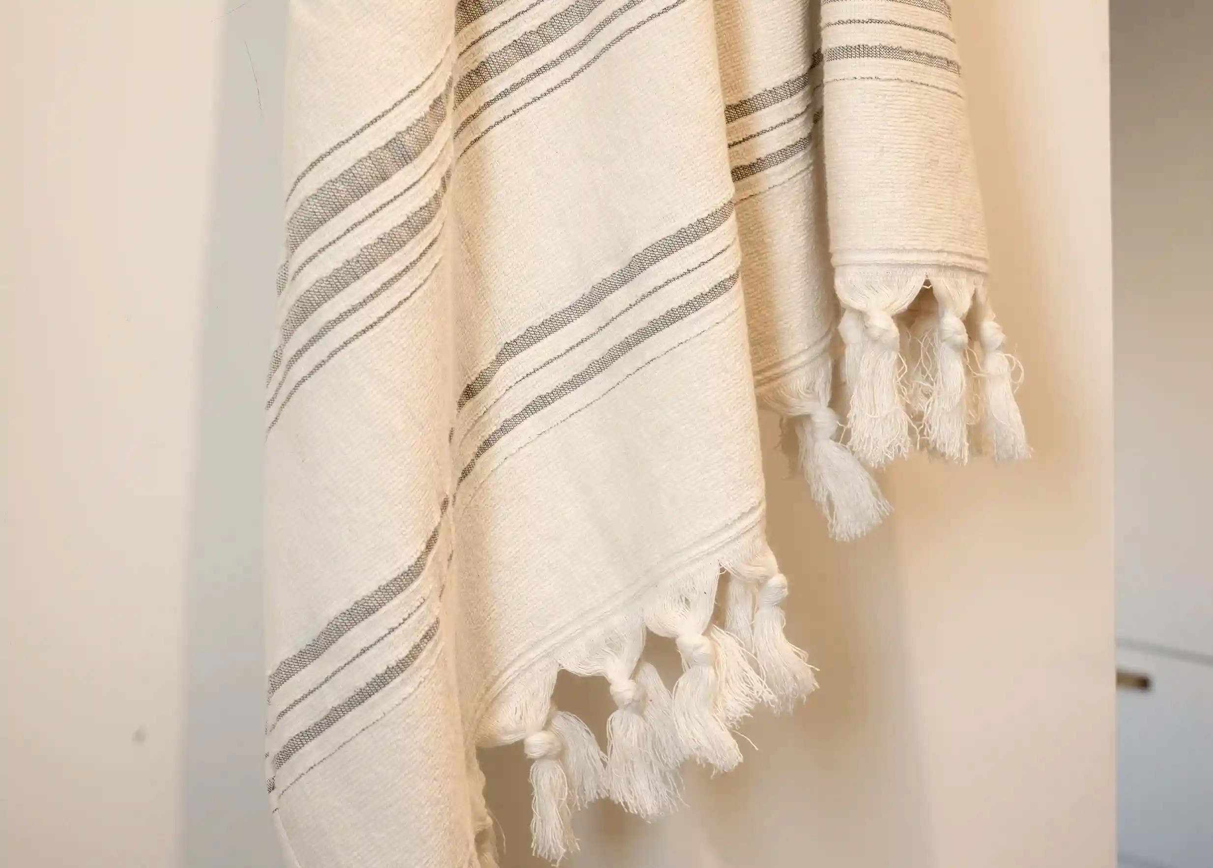Dolce Fouta au coloris Moonstone, vue de près, zoom sur les franges aux extrémités, nouées à la main, mur blanc d'arrière-plan