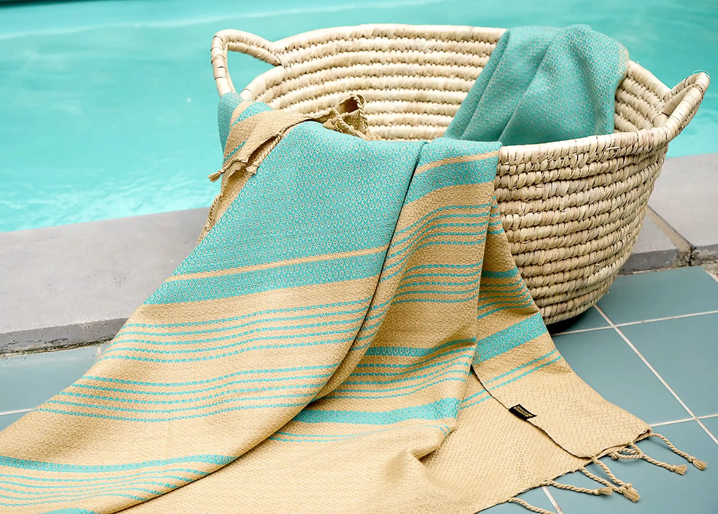 Aquasky-coloured fouta by Karawan authentic placed by the pool in a wicker basket