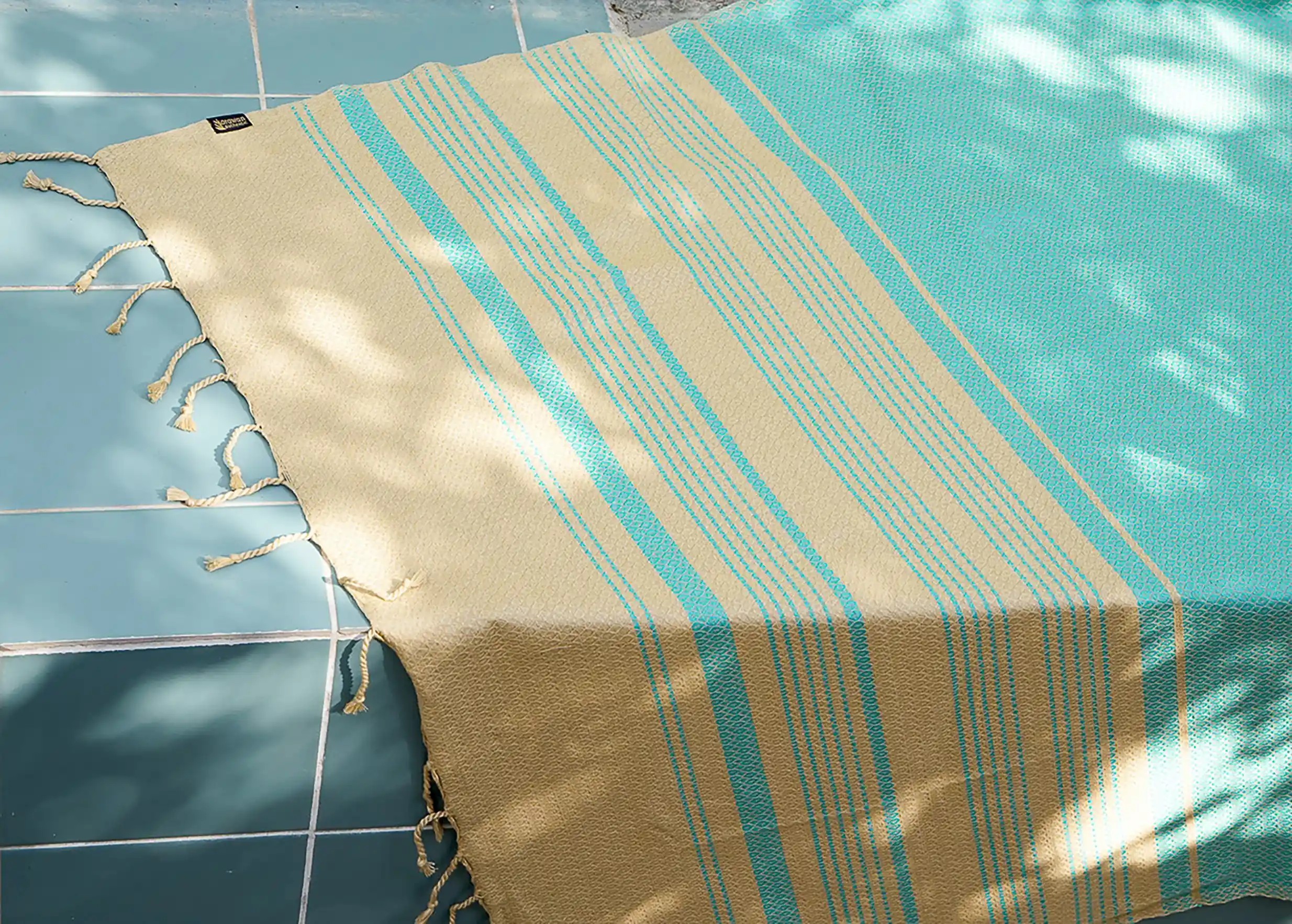 Aquasky-coloured fouta in organic cotton, Sand collection, spread out beside a swimming pool