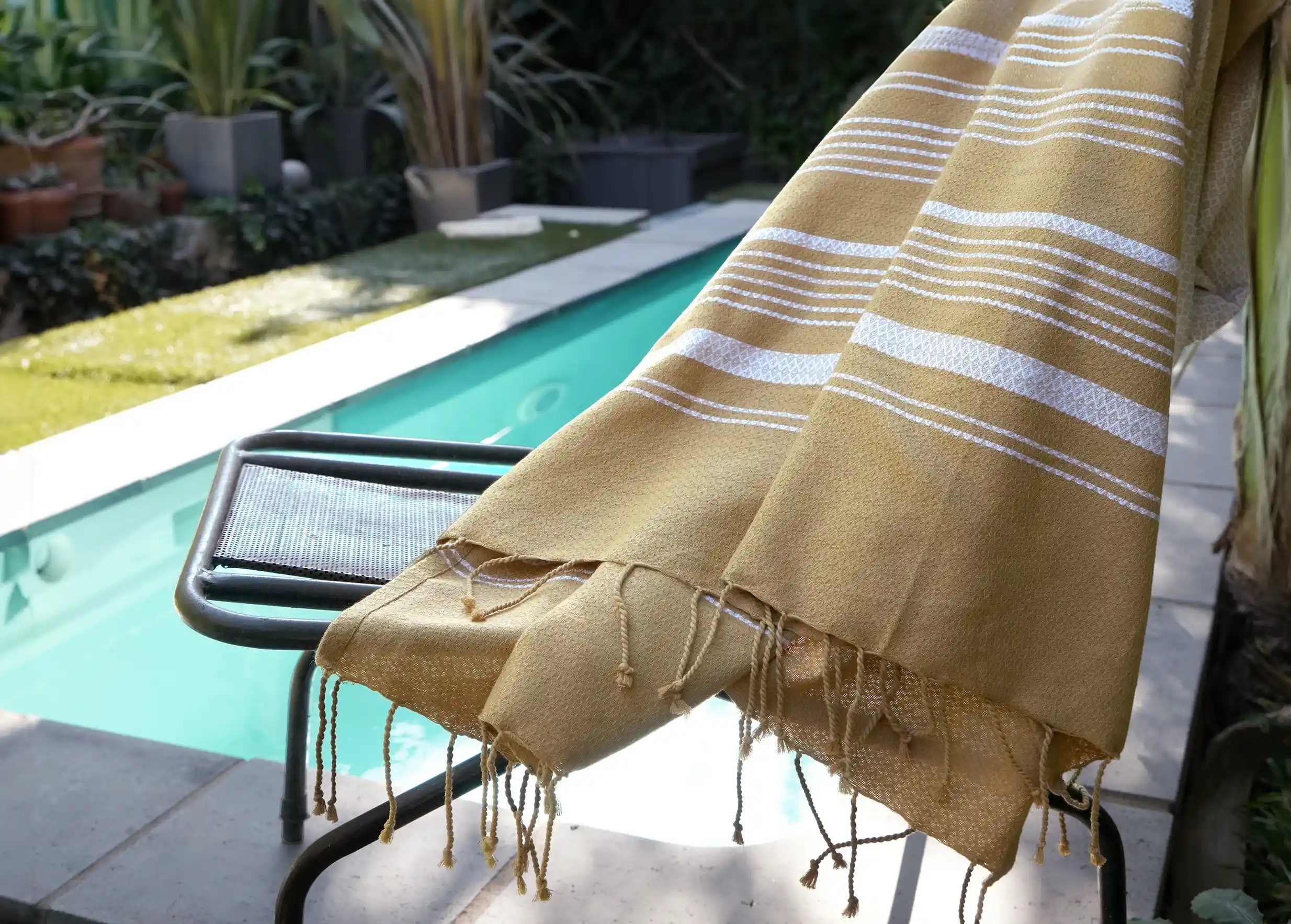 Fouta en coton bio blanc pur de la collection Sand, posée sur une chaise longue près d'une piscine par un temps ensoleillée