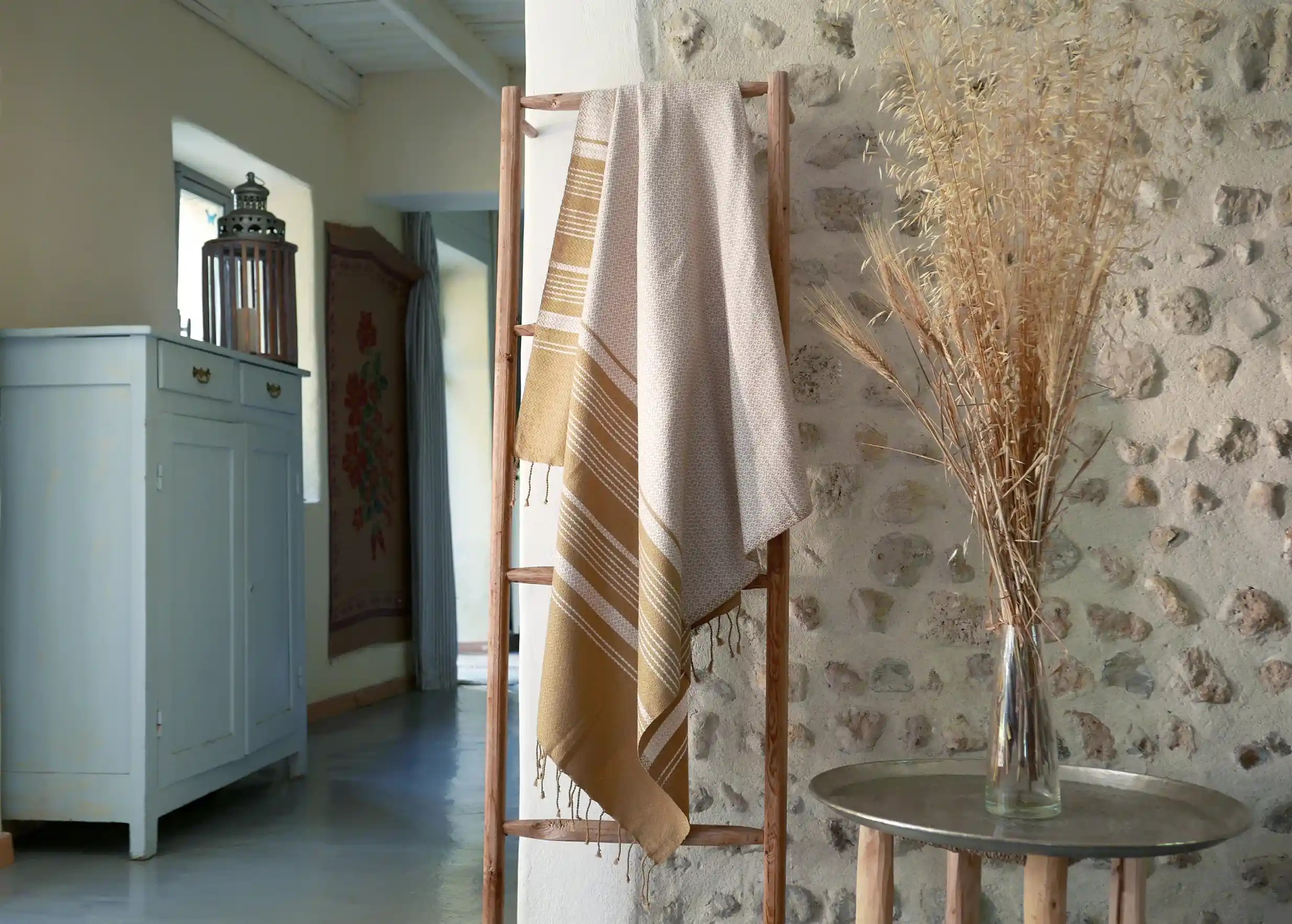 White organic cotton fouta with beige stripes, draped near a swimming pool, in front of a stone wall
