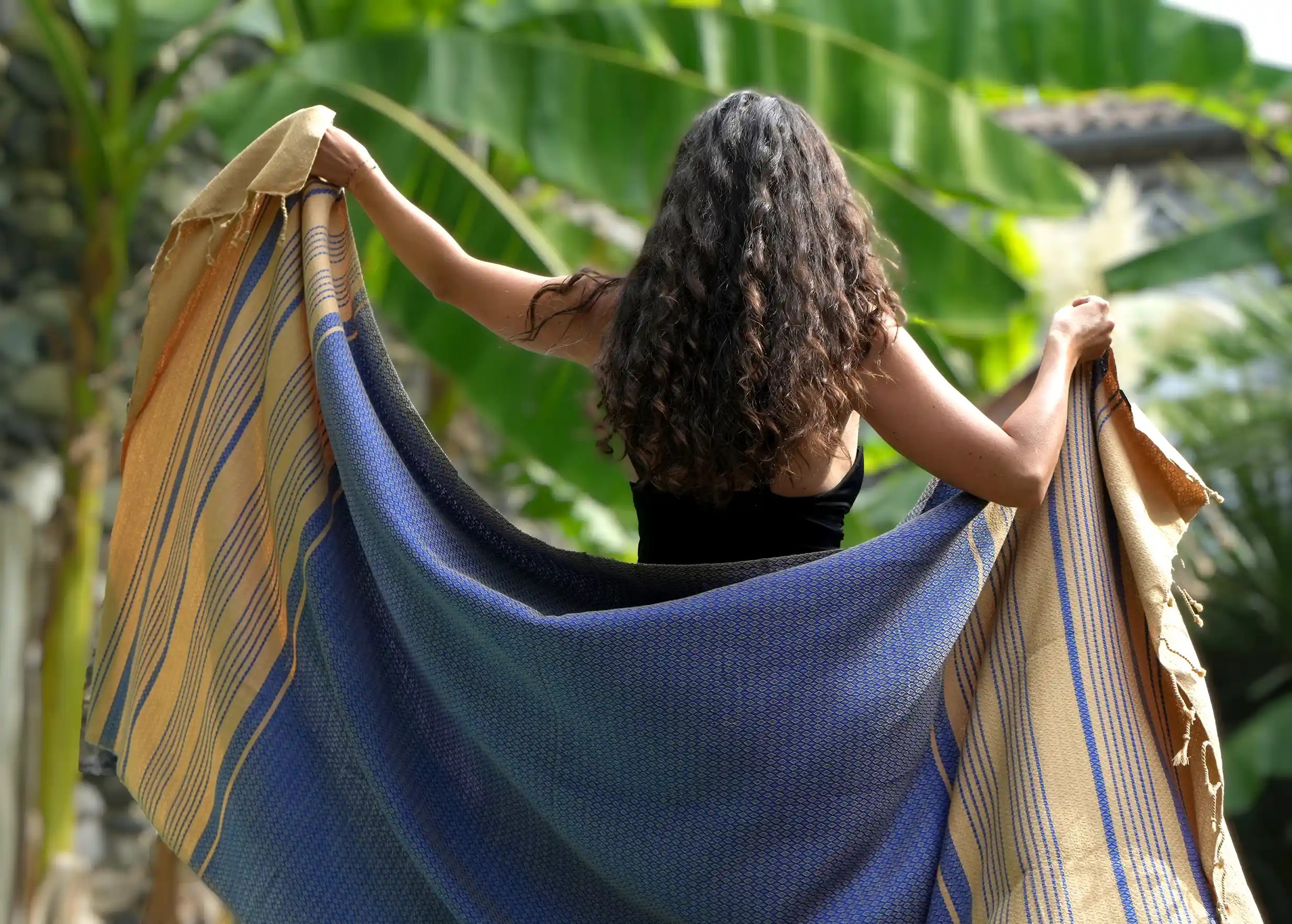 Femme de dos portant des deux bras une fouta en coton bleue de la collection Sand, rayures sableuses et tissage jacquard