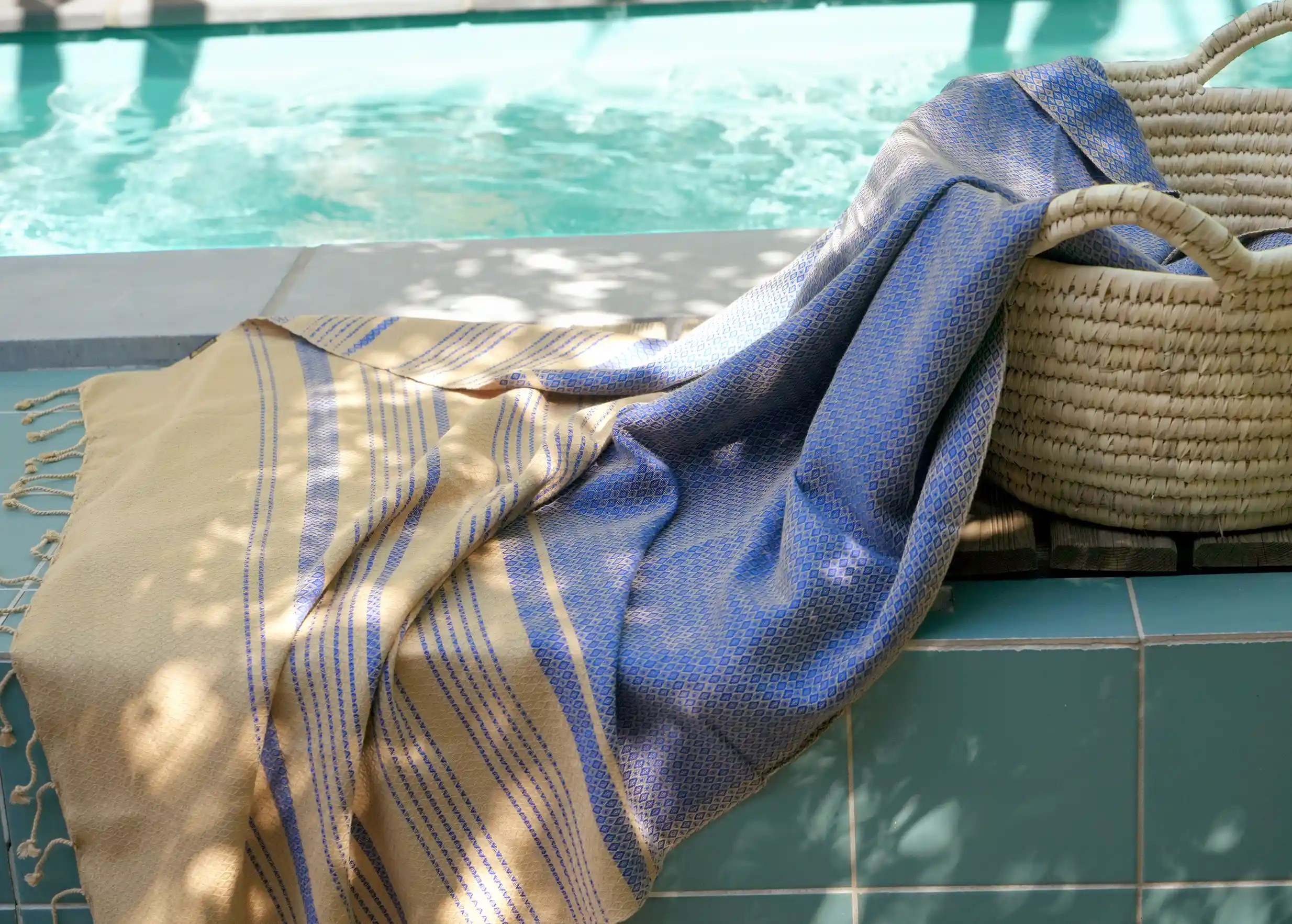 Fouta de la collection Sand, coloris bleu impérial, étalée près d'un rebord de piscine, avec un panier en osier