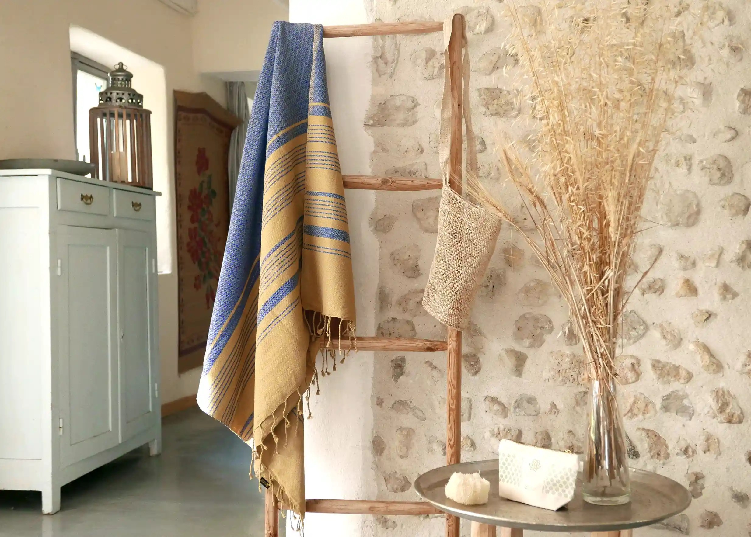 Fouta bleu impérial accrochée à une échelle en bois, plante déco et mur en pierre