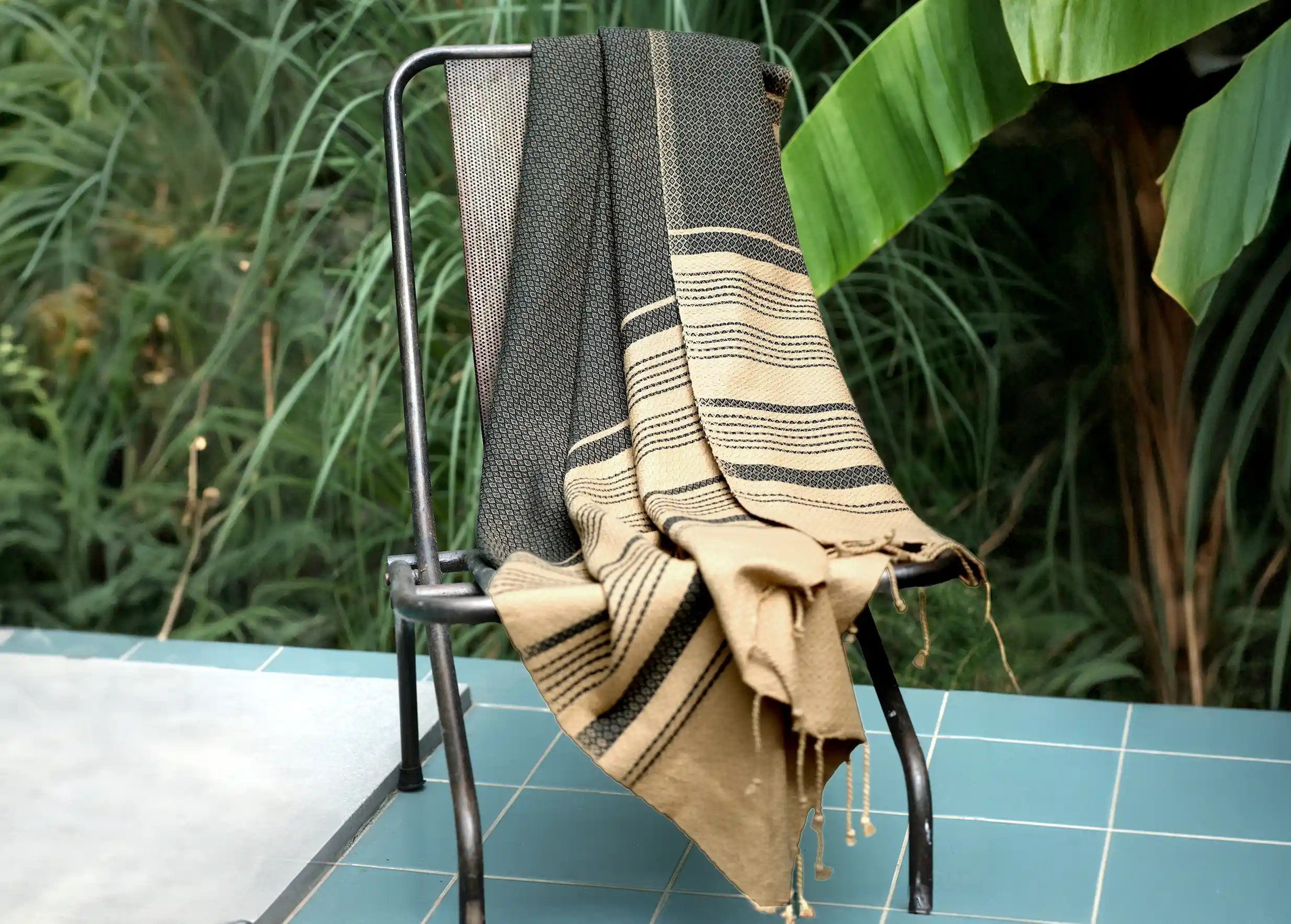 Ash-coloured fouta in organic cotton, on a black metal chair, plants in the background