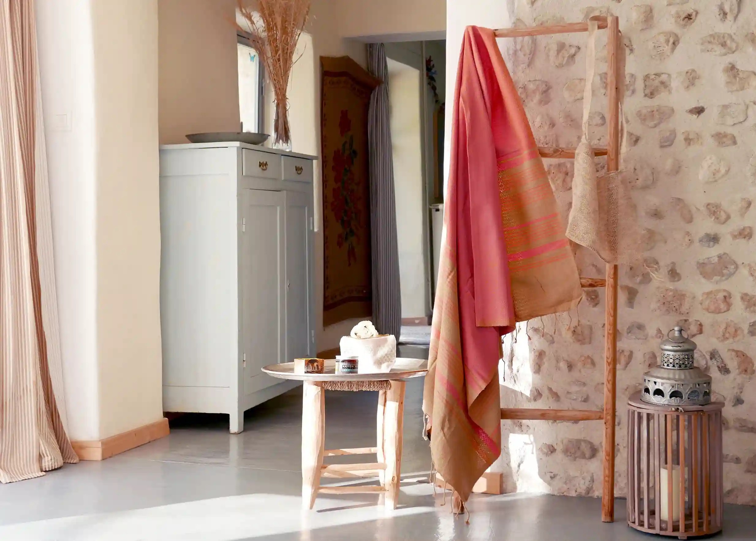 Indian pink coloured fouta, Sand collection, hung side by side against a stone wall, with a decorative plant next to them.